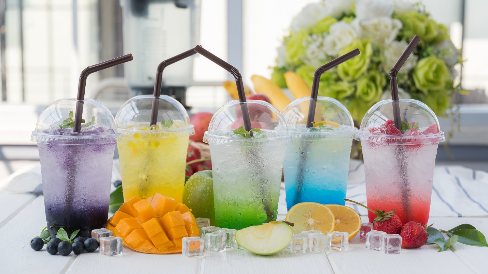 Коктейли в стаканах с трубочками на столе с кубиками льда и фруктами