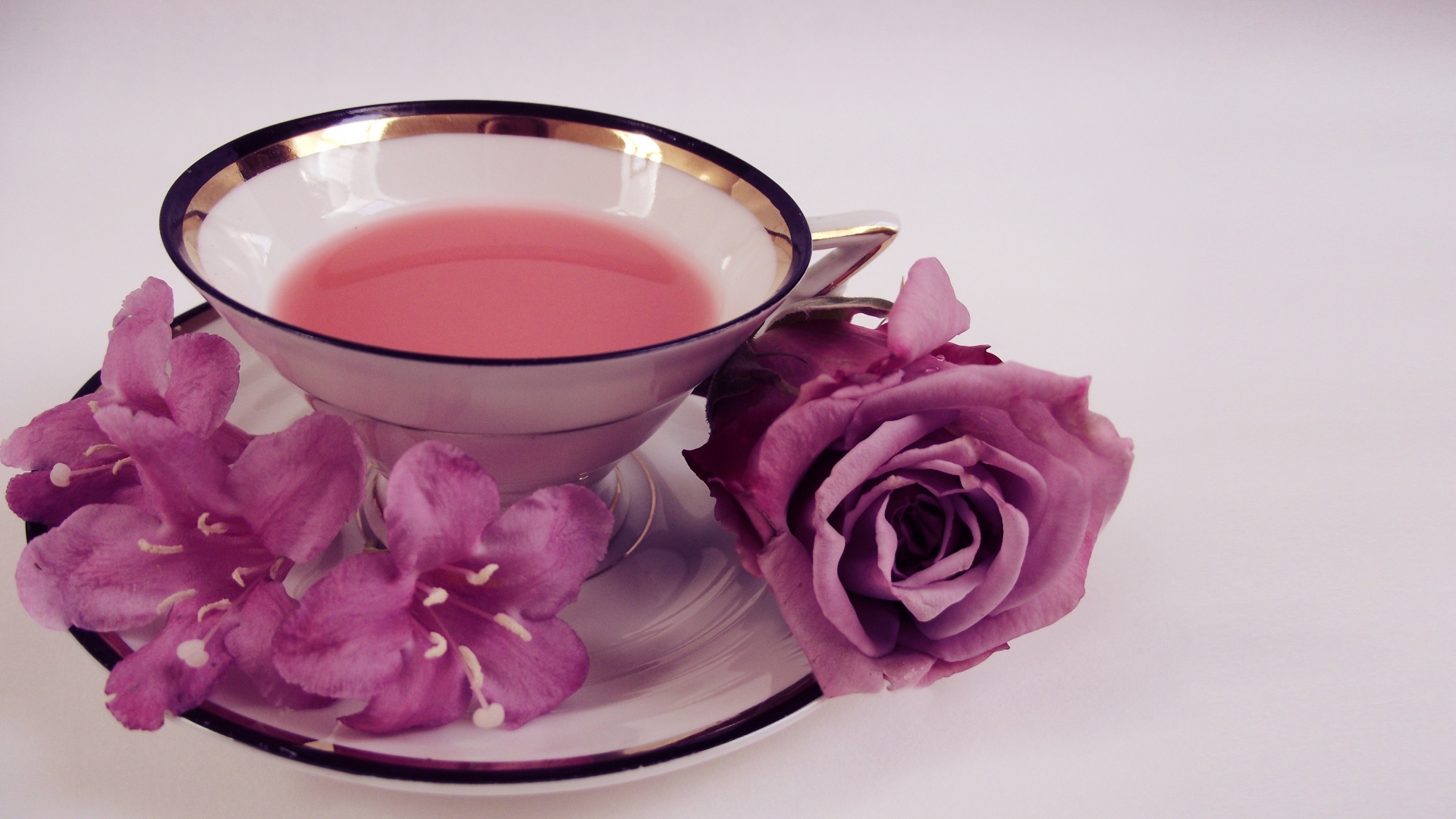 Чашка чаю на тарелке с розой и колокольчиками на сером фоне