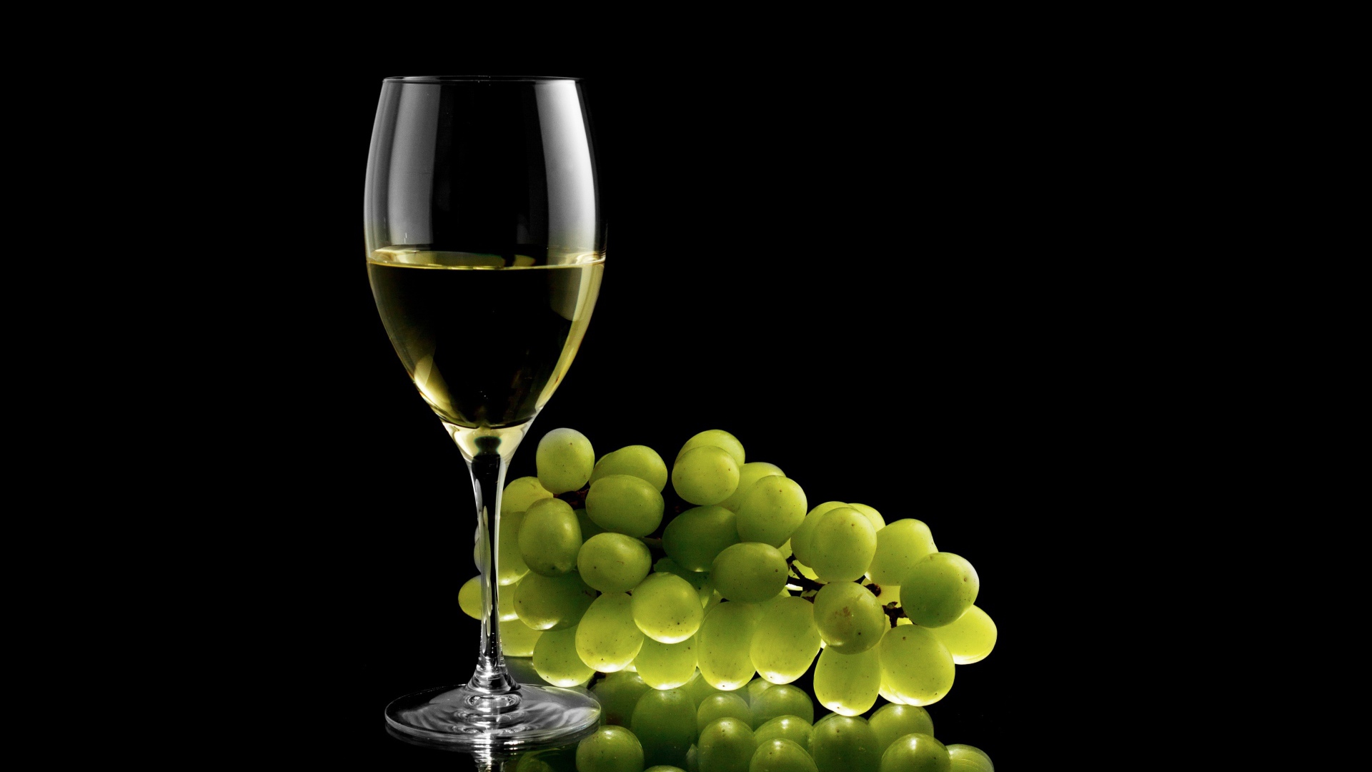 Glass of white wine with white grapes on a black background