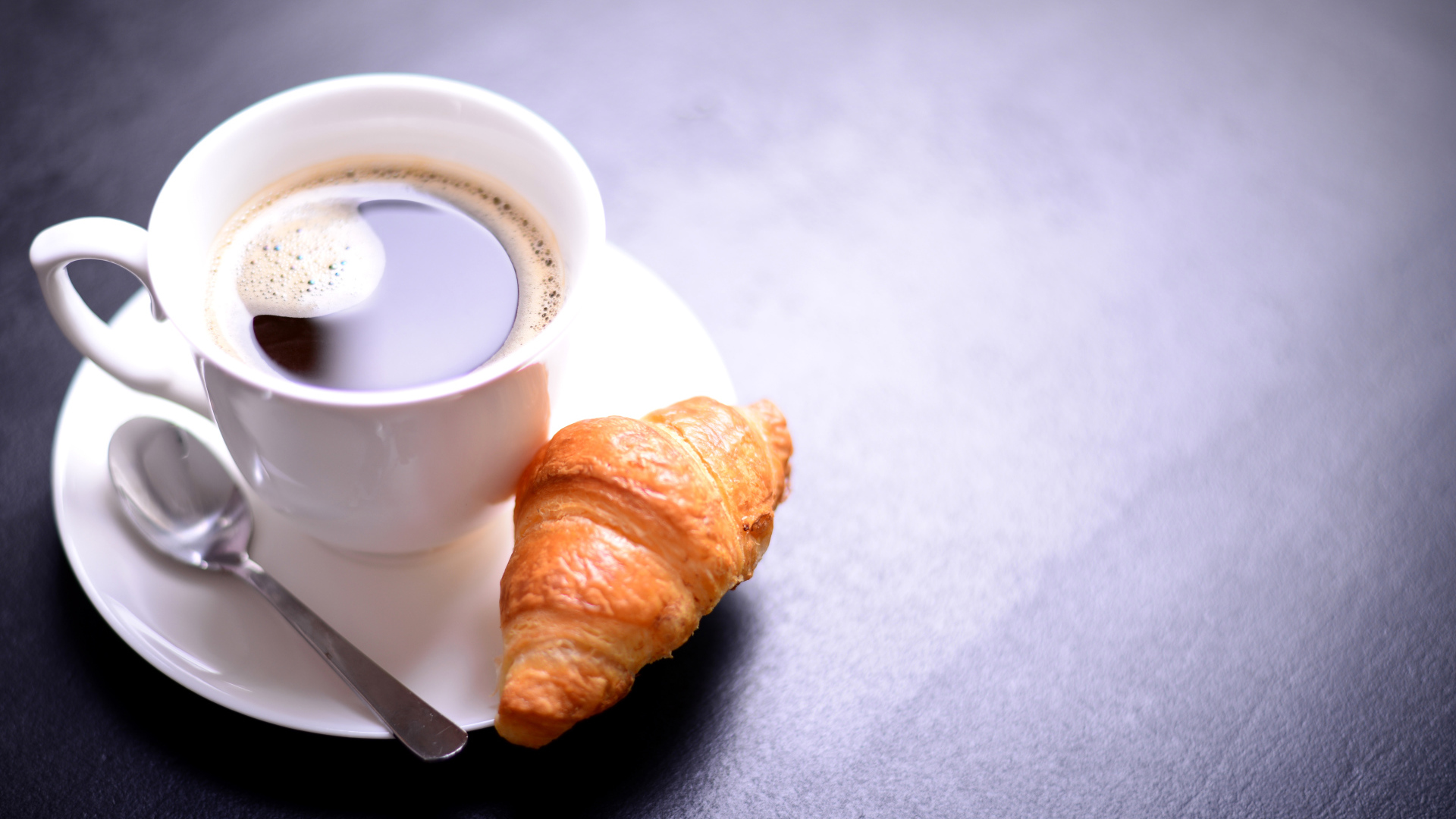 Белая чашка кофе на столе с круассаном