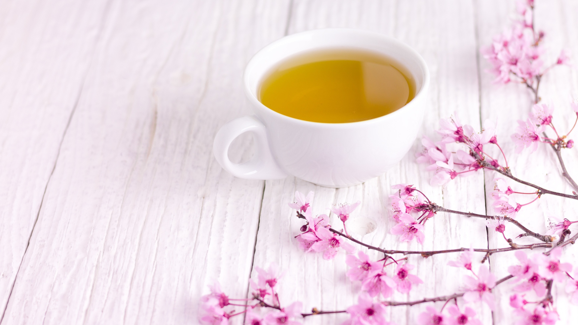 Белая чашка зеленого чая на столе с розовыми цветами