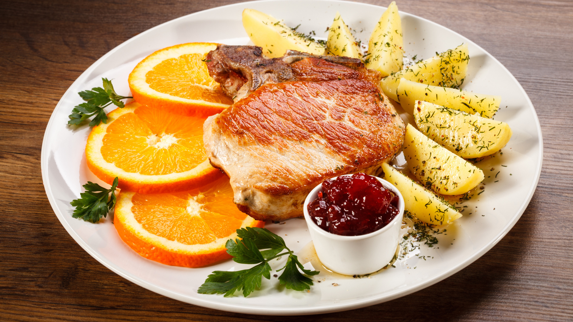 Кусок запеченного мяса с кусочками картофеля и апельсина и соусом