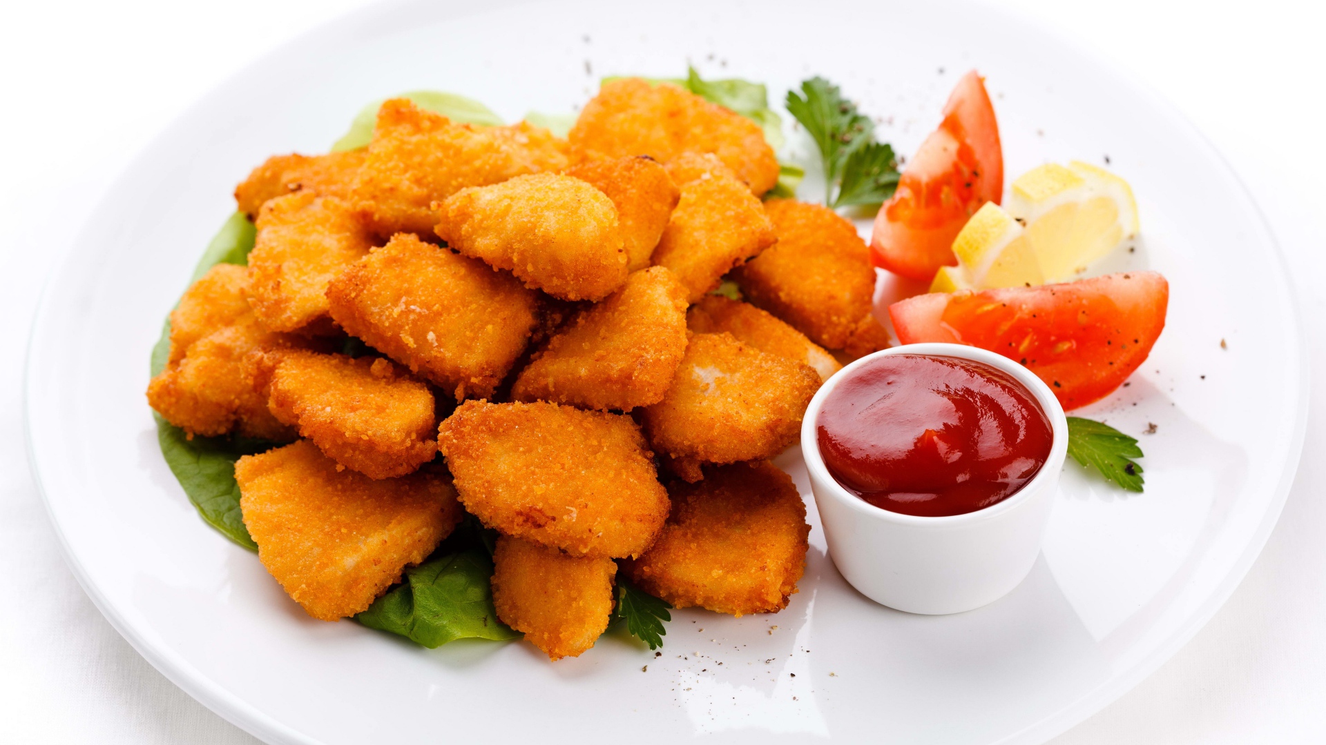 Куриные наггетсы с соусом и помидорами на белой тарелке 