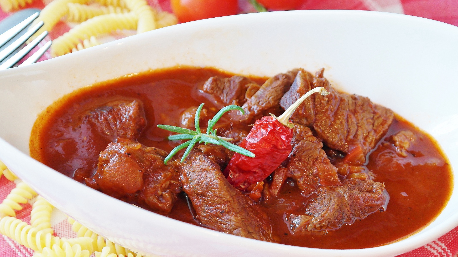 Мясной гуляш в белой тарелке с острым перцем