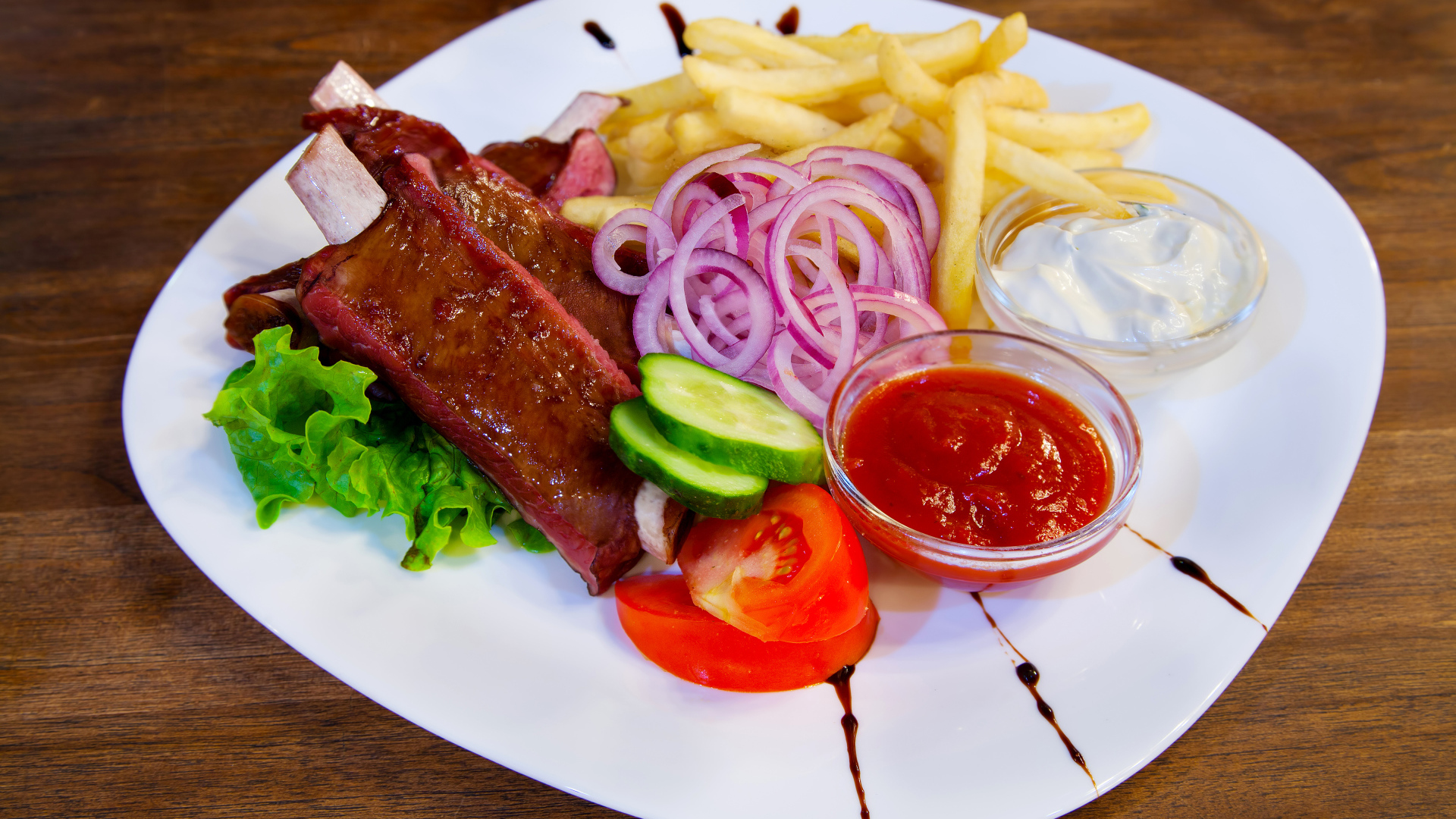 Мясо с овощами и картофелем фри на большой белой тарелке с соусом