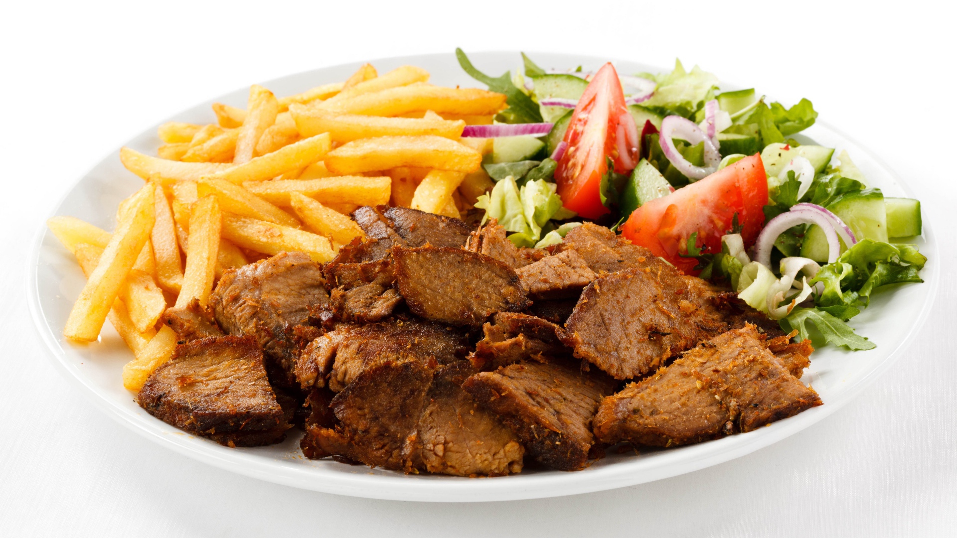 Кусочки мяса на тарелке с картофелем фри и салатом