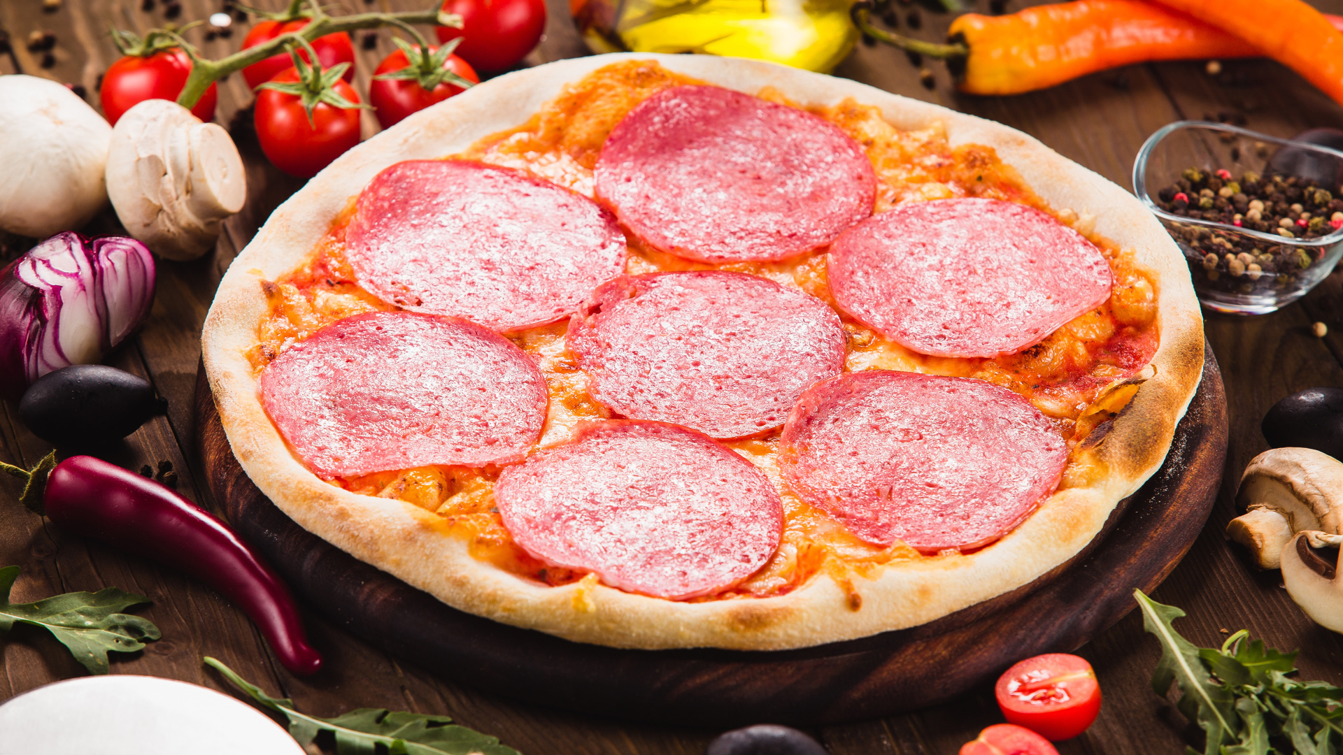 Пицца с салями на столе с овощами 