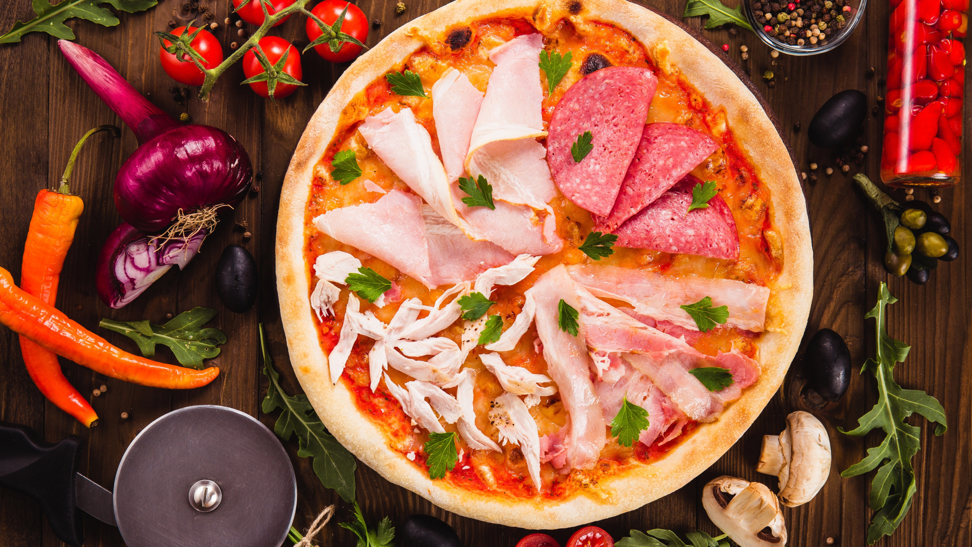 Пицца с колбасой, курицей и кусочками ветчины на столе с овощами 