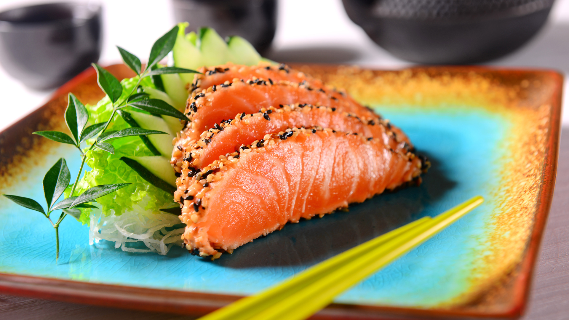 Красная рыба с листьями салата и свежими огурцами на тарелке с палочками