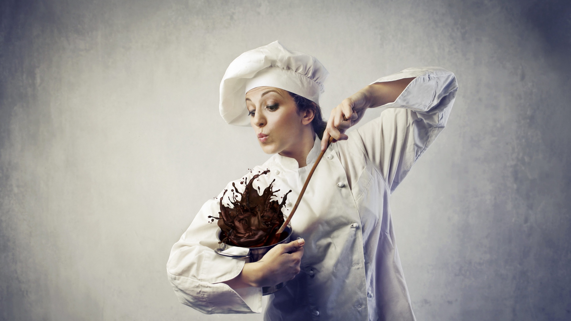 Женщина повар мешает шоколад в посуде на сером фоне