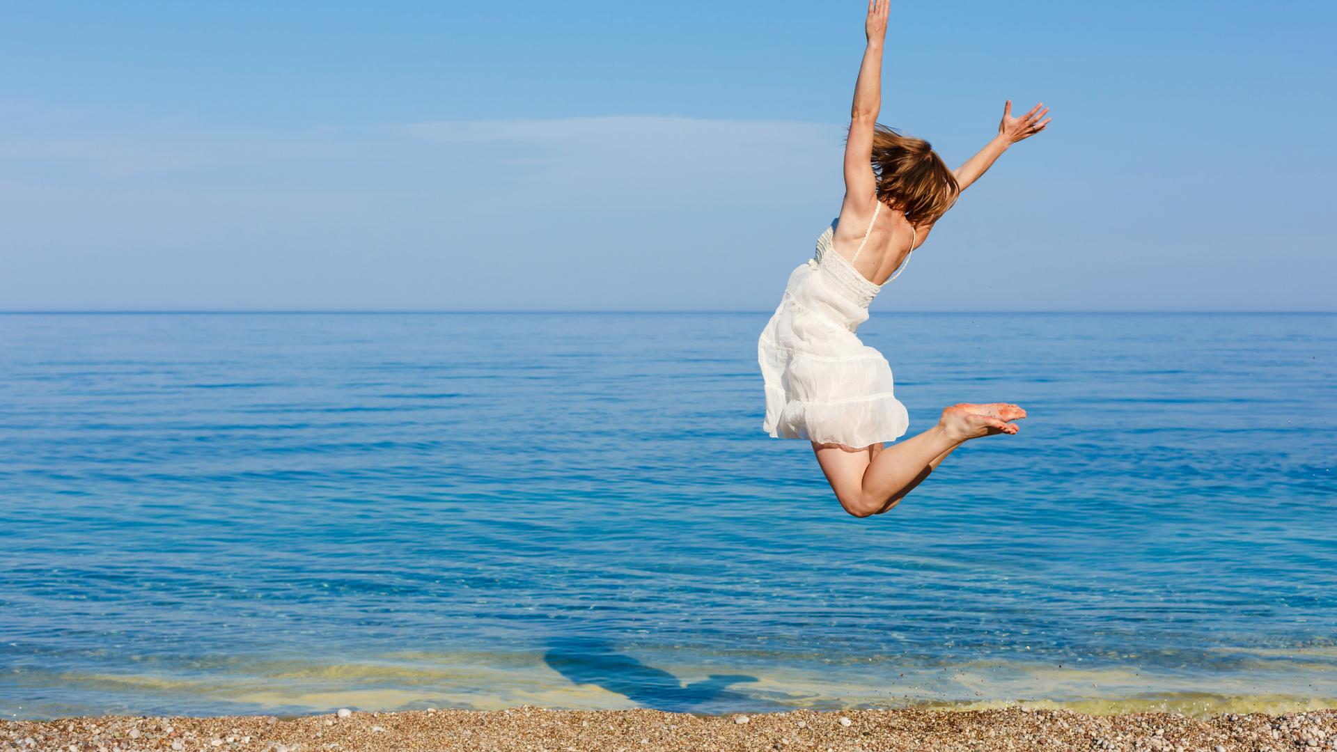 Молодая девушка в белом платье делаем прыжок на песке у моря