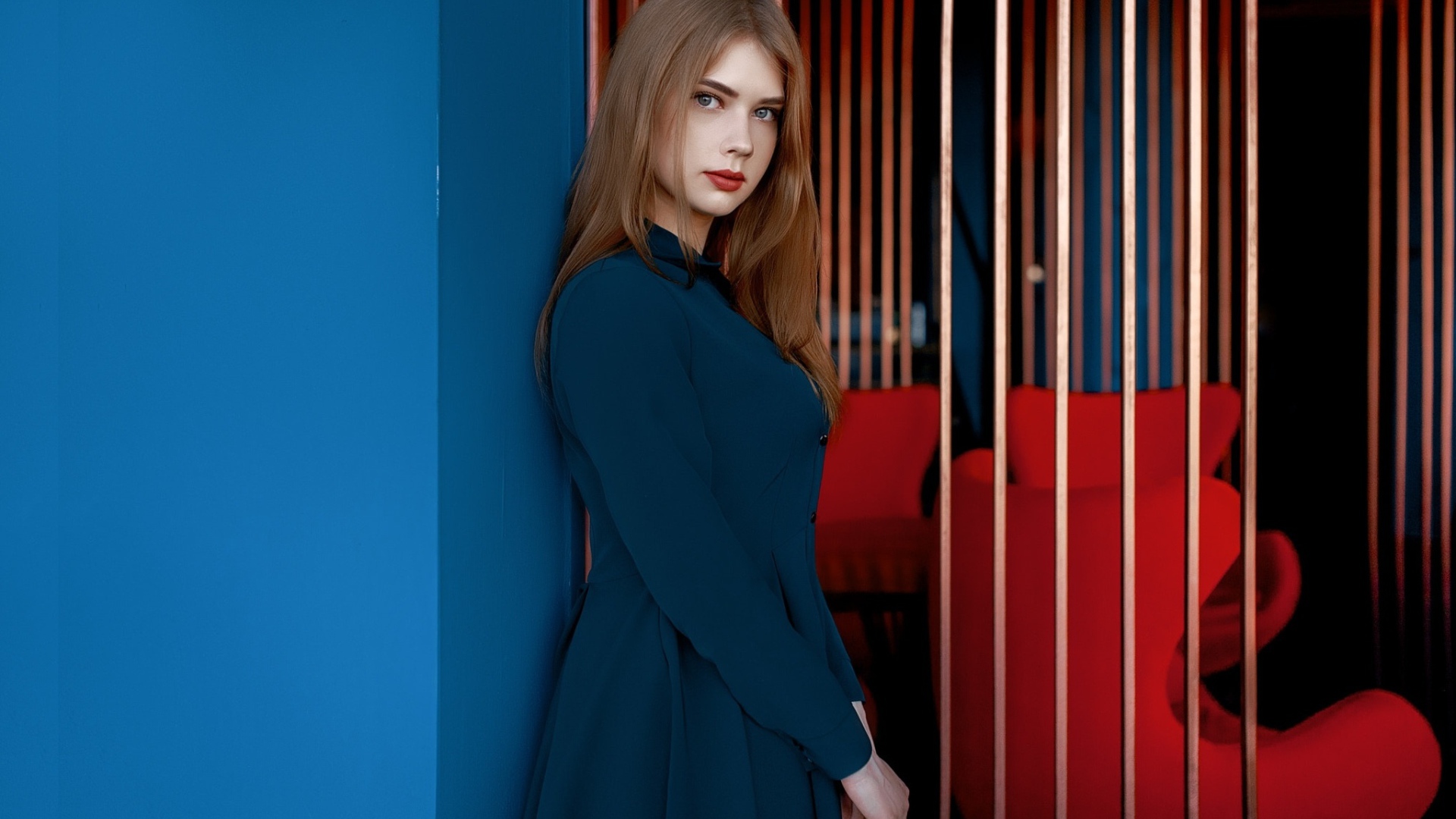 Красивая голубоглазая девушка стоит в пальто у стены