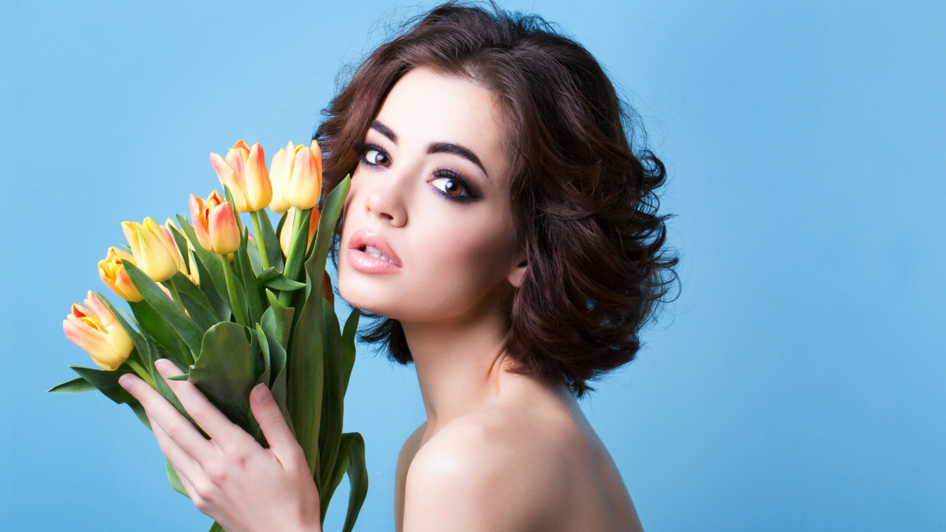 Красивая девушка брюнетка с букетом тюльпанов на голубом фоне