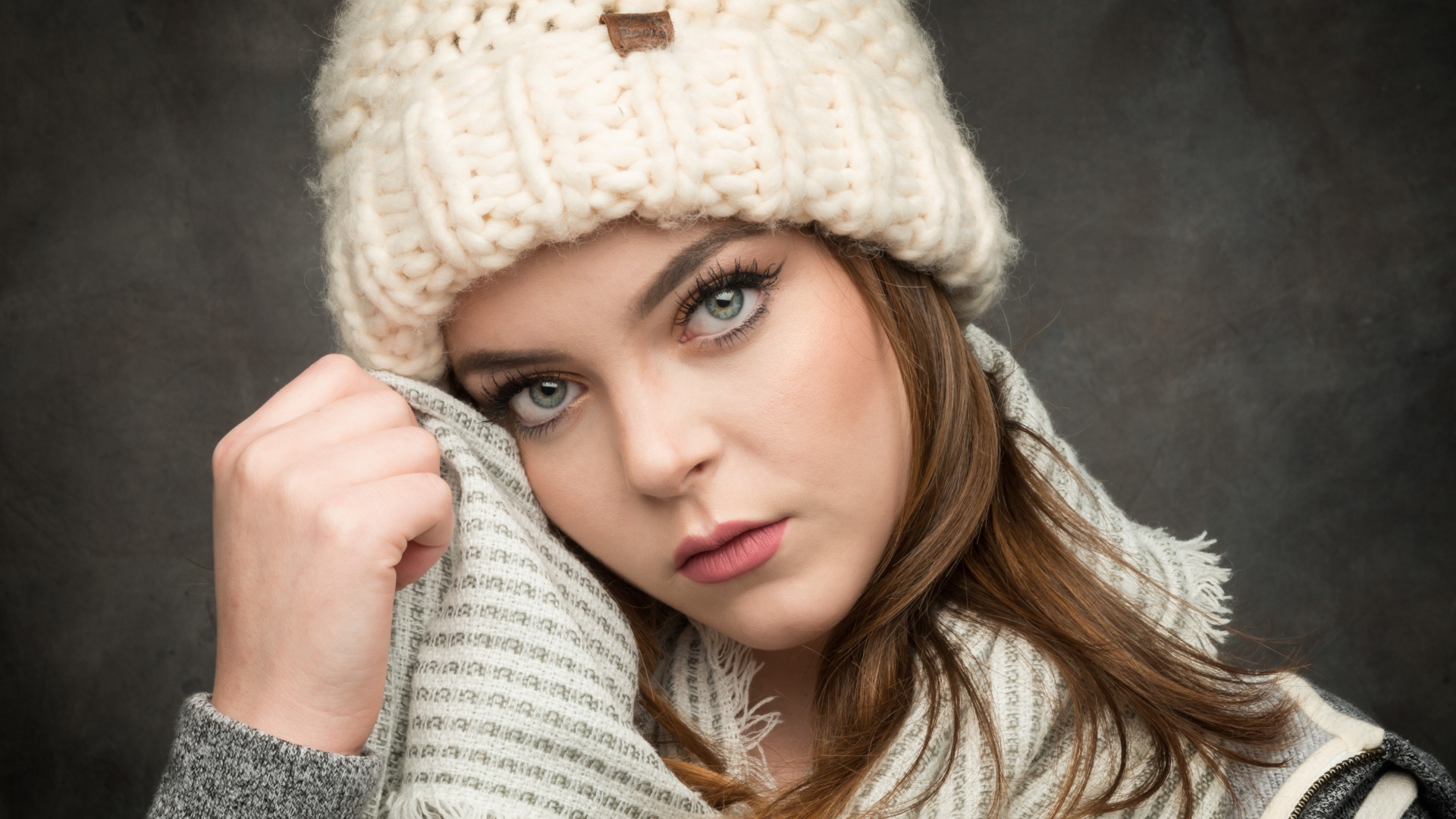 Красивая зеленоглазая девушка в белой вязаной шапке с шарфом