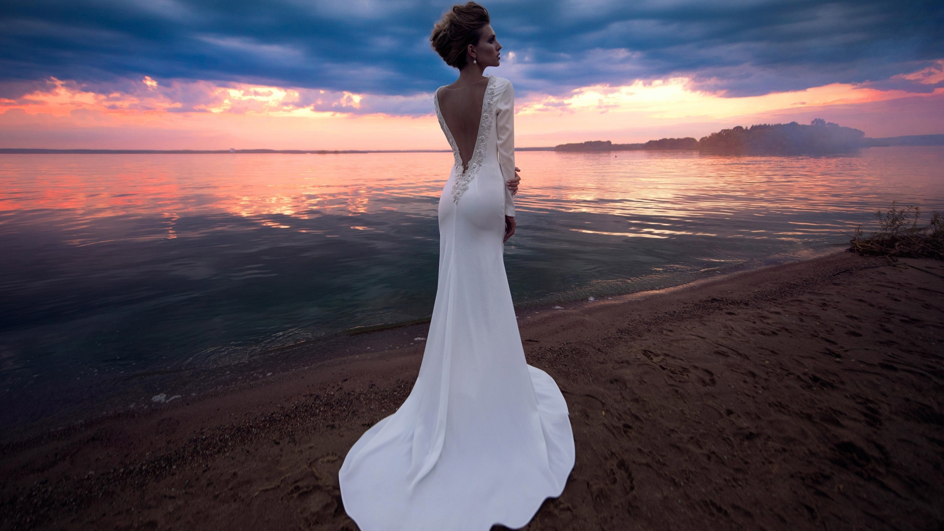 Красивая молодая девушка в свадебном платье у воды на закате 