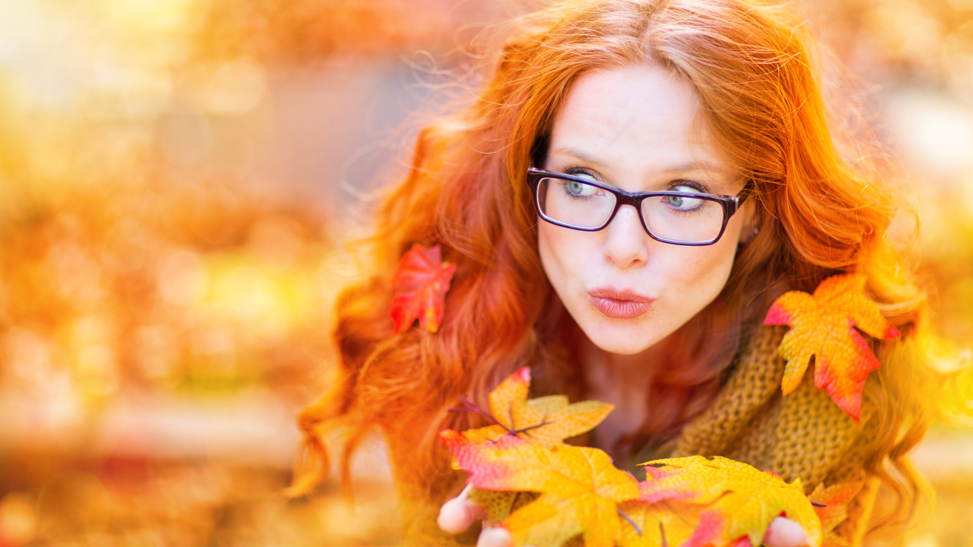 Рыжеволосая девушка в очках держит в руках опавшие листья 