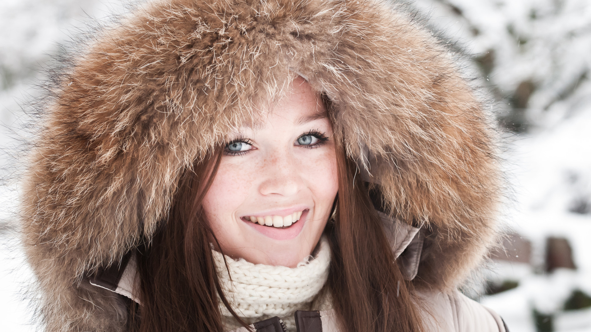 Улыбающаяся голубоглазая девушка в капюшоне зимой