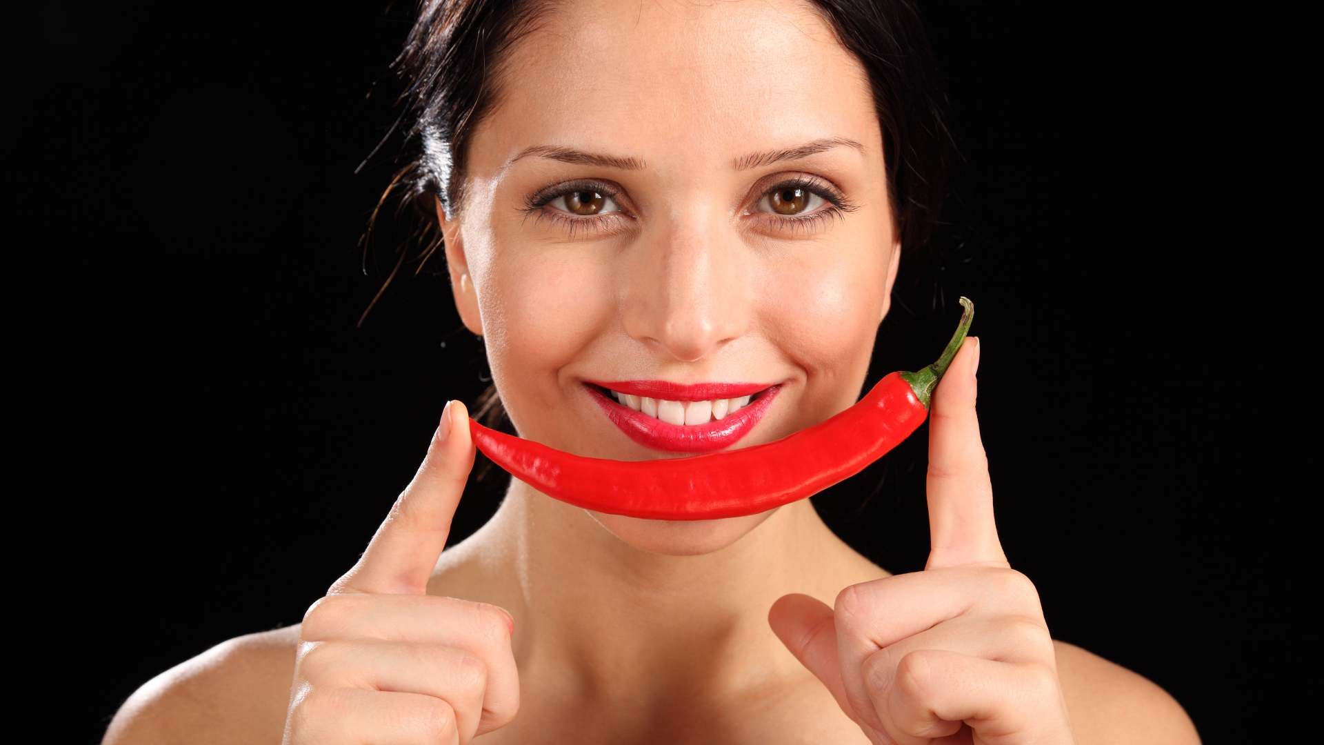 Улыбающаяся девушка с красным перцем на черном фоне
