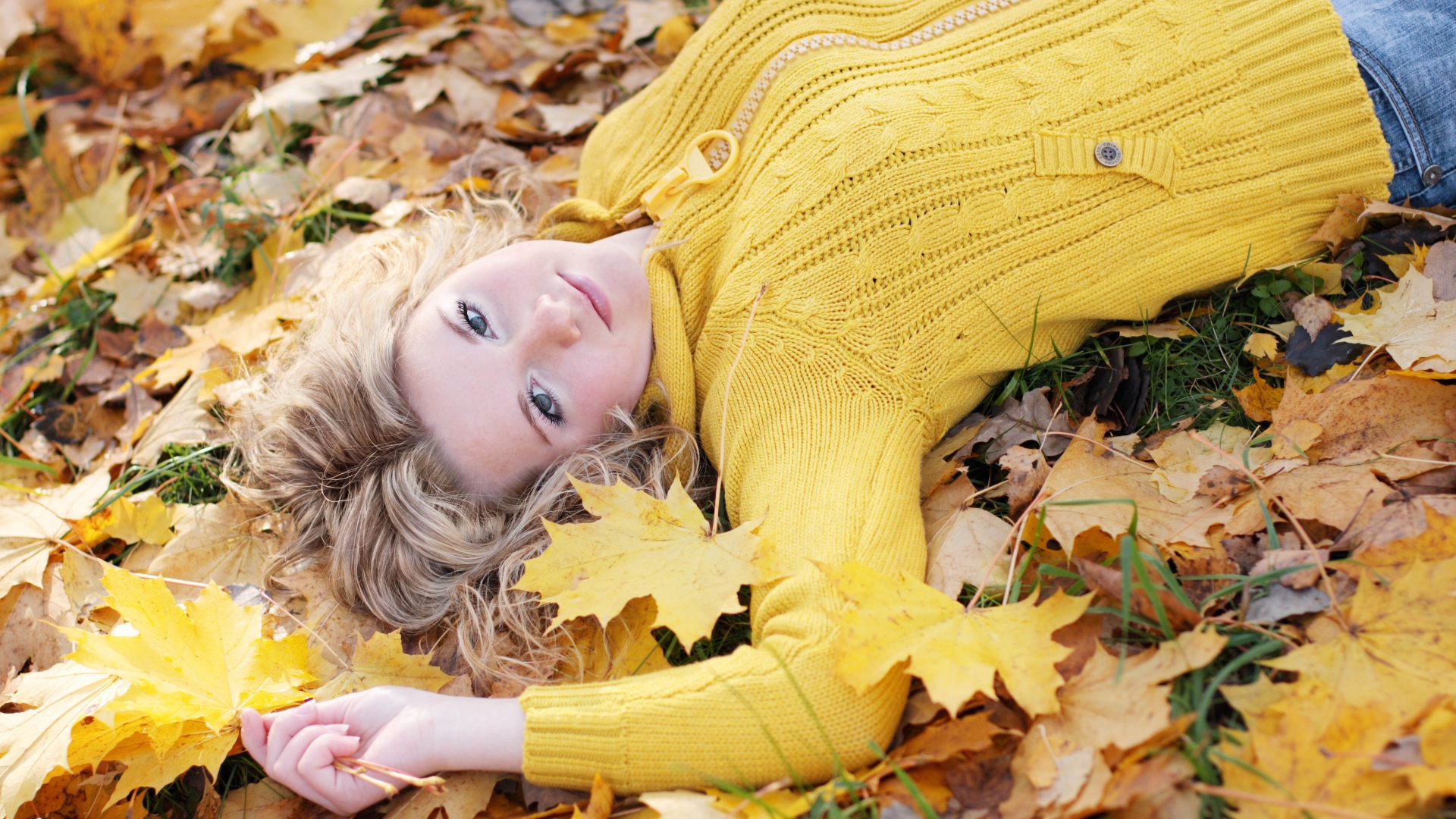 Молодая блондинка лежит на сухой листве осенью