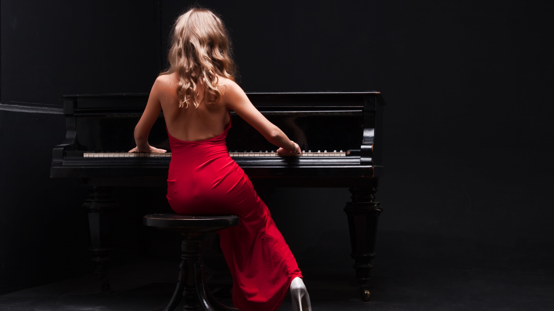 Молодая девушка в красном платье играет на пианино