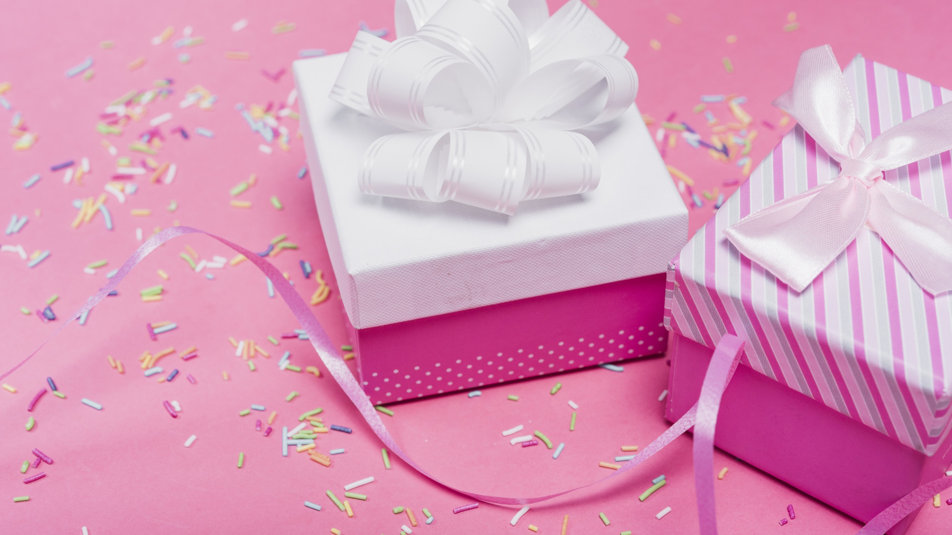 Две подарочные коробки с бантами на розовом фоне