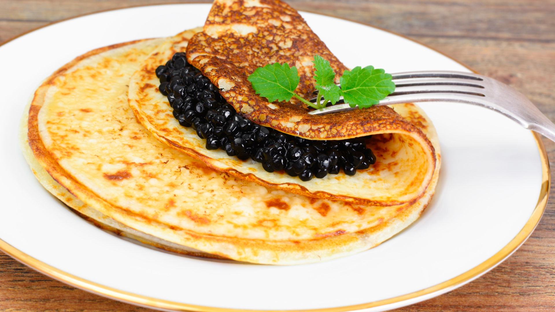 Блины с черной икрой на тарелке с вилкой