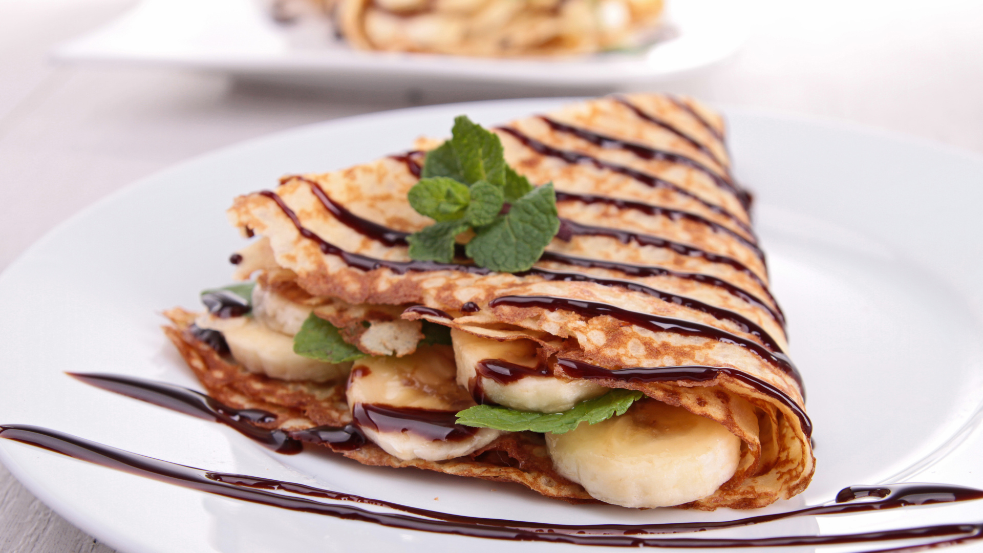 Тонкие сладкие блины с бананами и шоколадом на белой большой тарелке угощение на Масленицу