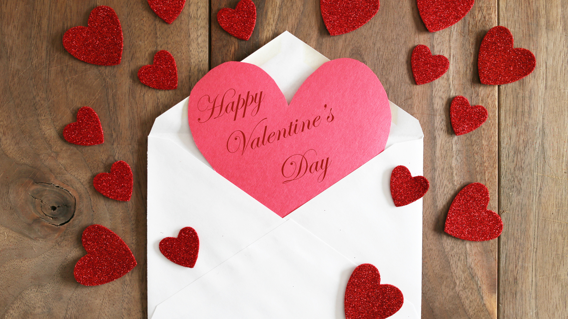 Белый конверт с валентинкой на деревянном столе с красными сердечками на 14 февраля
