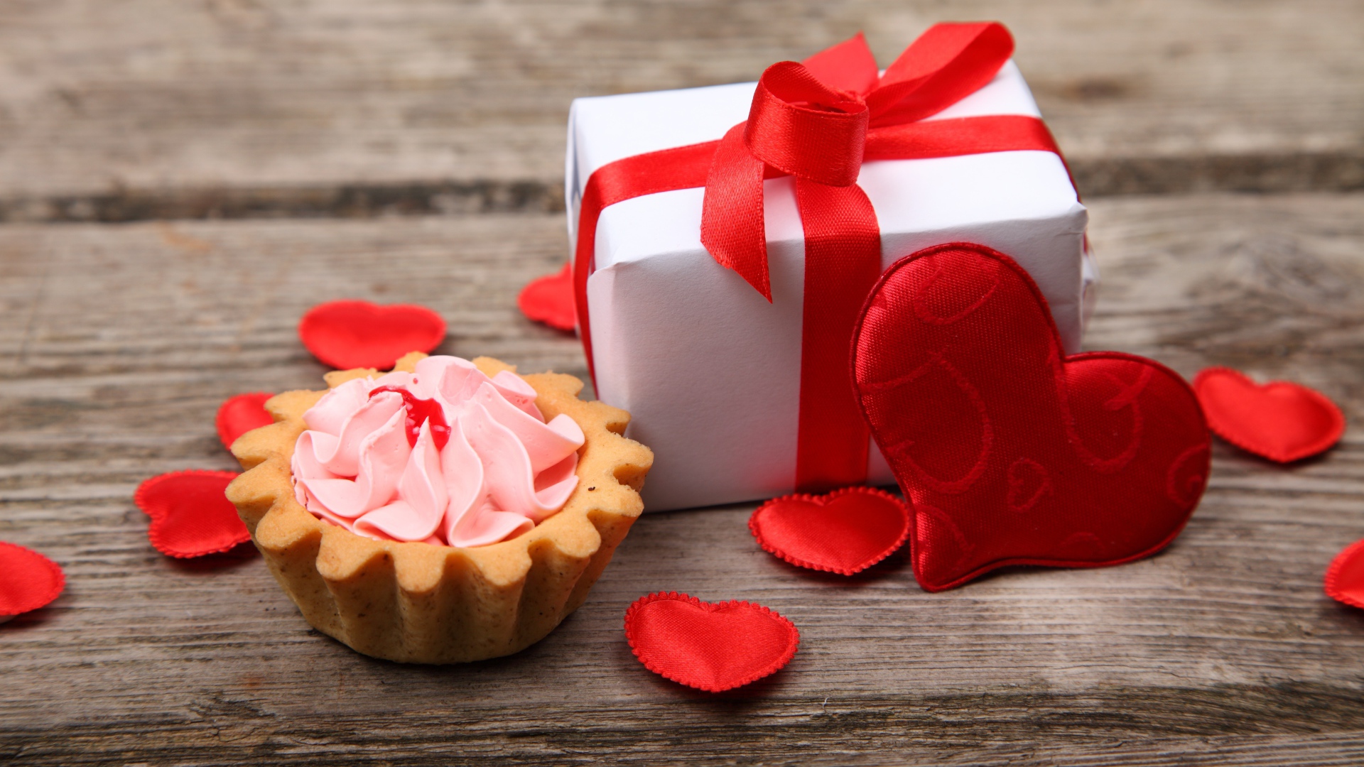 Подарок с красными сердечками и пирожным на столе
