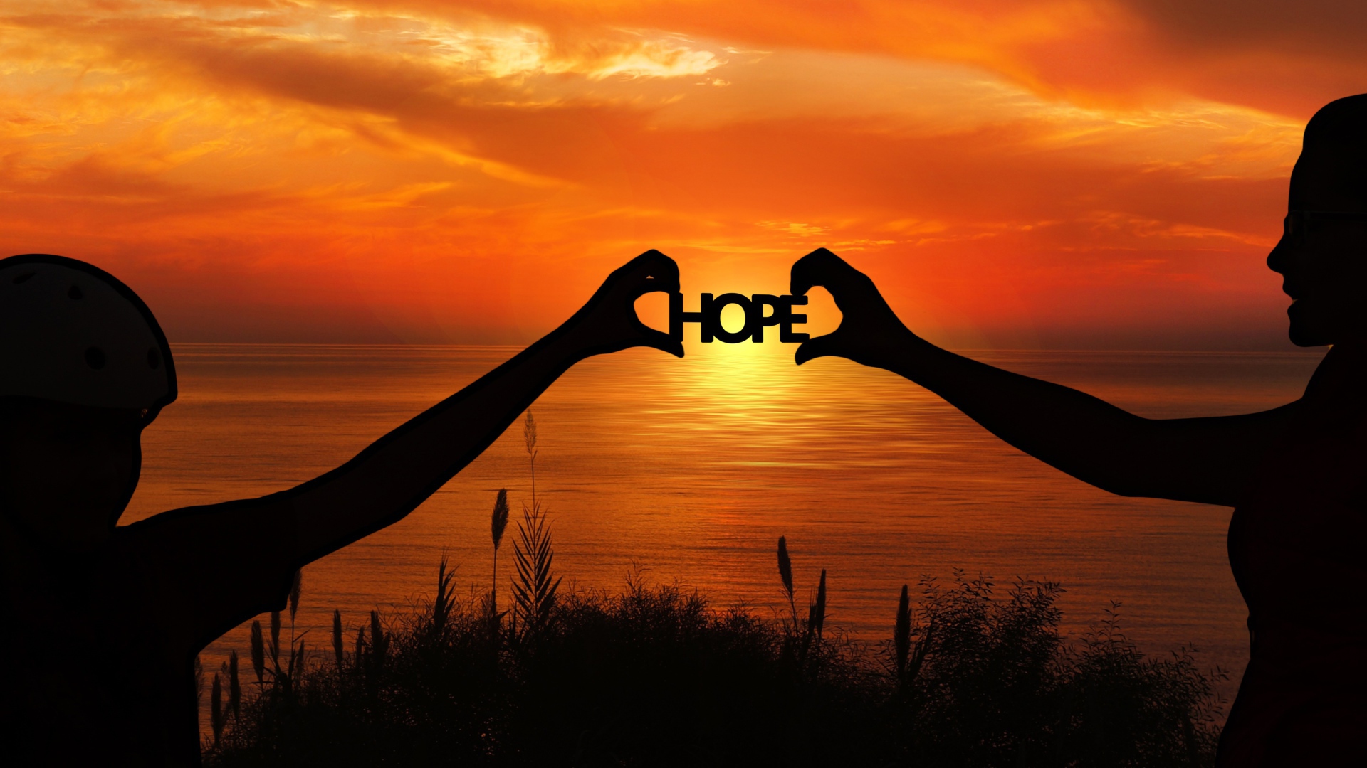 Силуэты пары держат в руках надпись HOPE на фоне заката