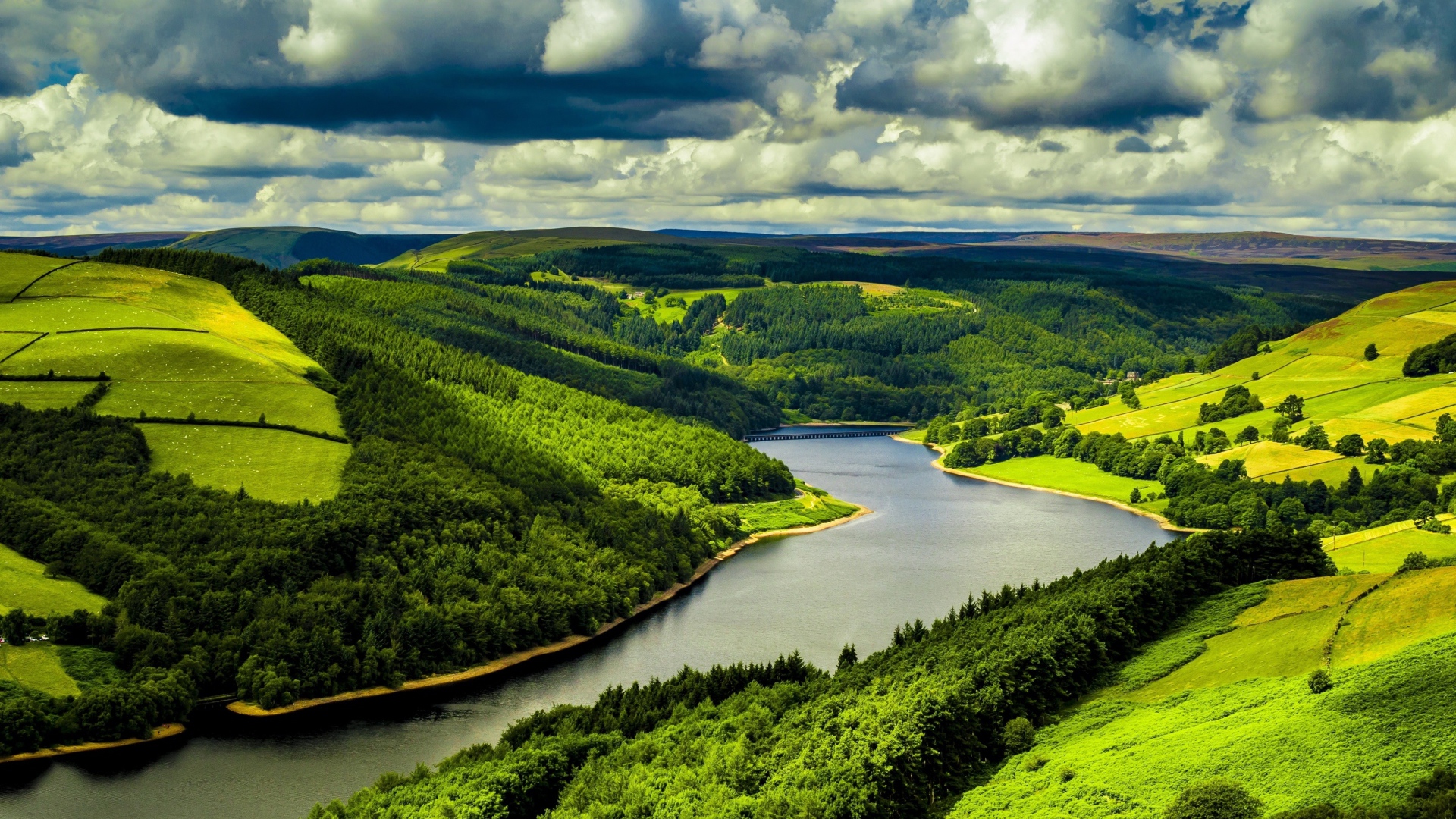 Зеленые холмы у реки под небом с густыми белыми облаками