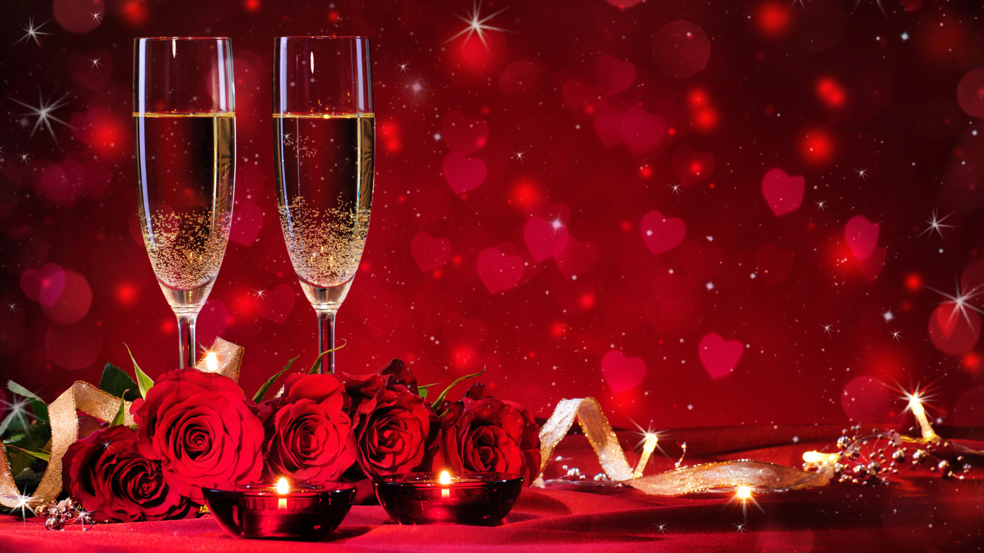 Букет роз и два фужера шампанского с зажженными свечами на красном фоне