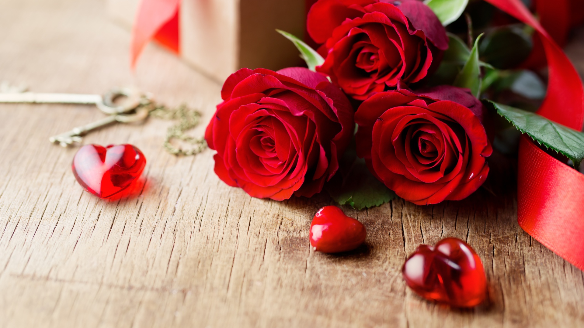 Три красных розы на деревянном столе с красными сердечками