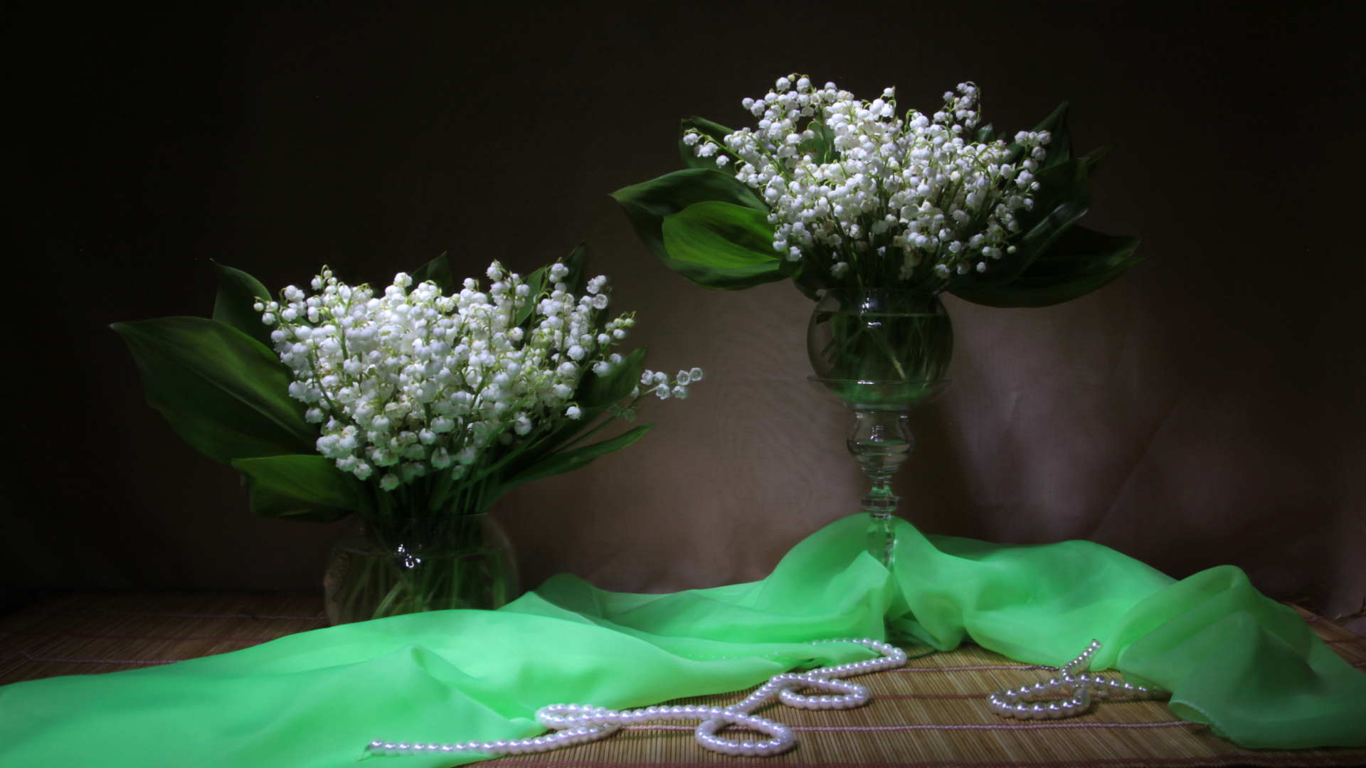 Два букета ландышей с бусами на столе 