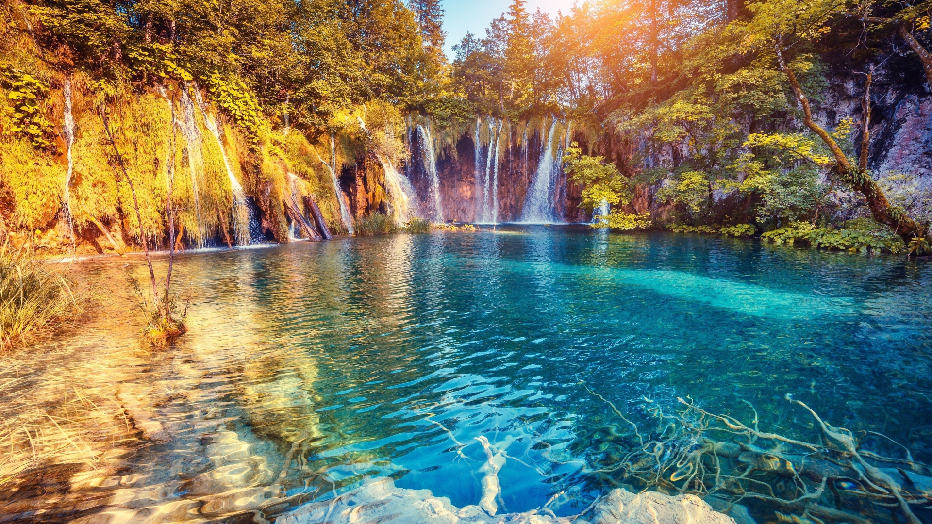 Водопад в лучах солнца стекает со скалы в реку