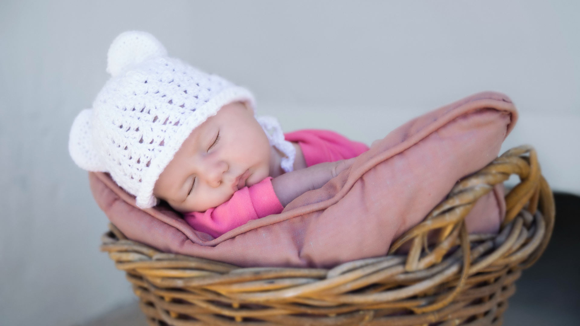 Маленький ребенок в белой шапке спит в корзине