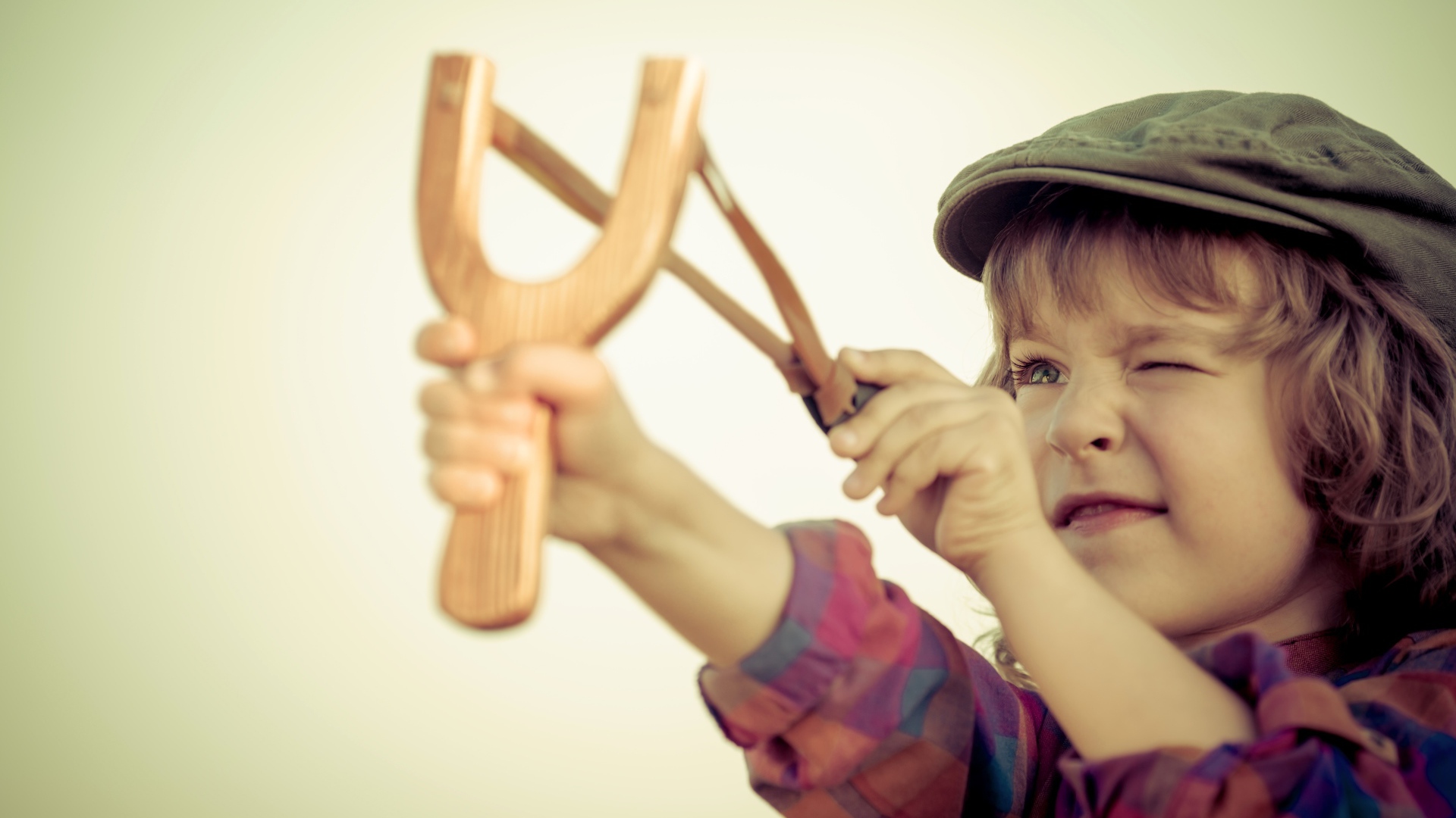 Маленький мальчик в кепке целится с рогатки