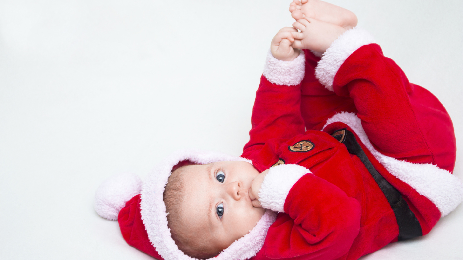 Маленький ребенок в красном новогоднем костюме на сером фоне