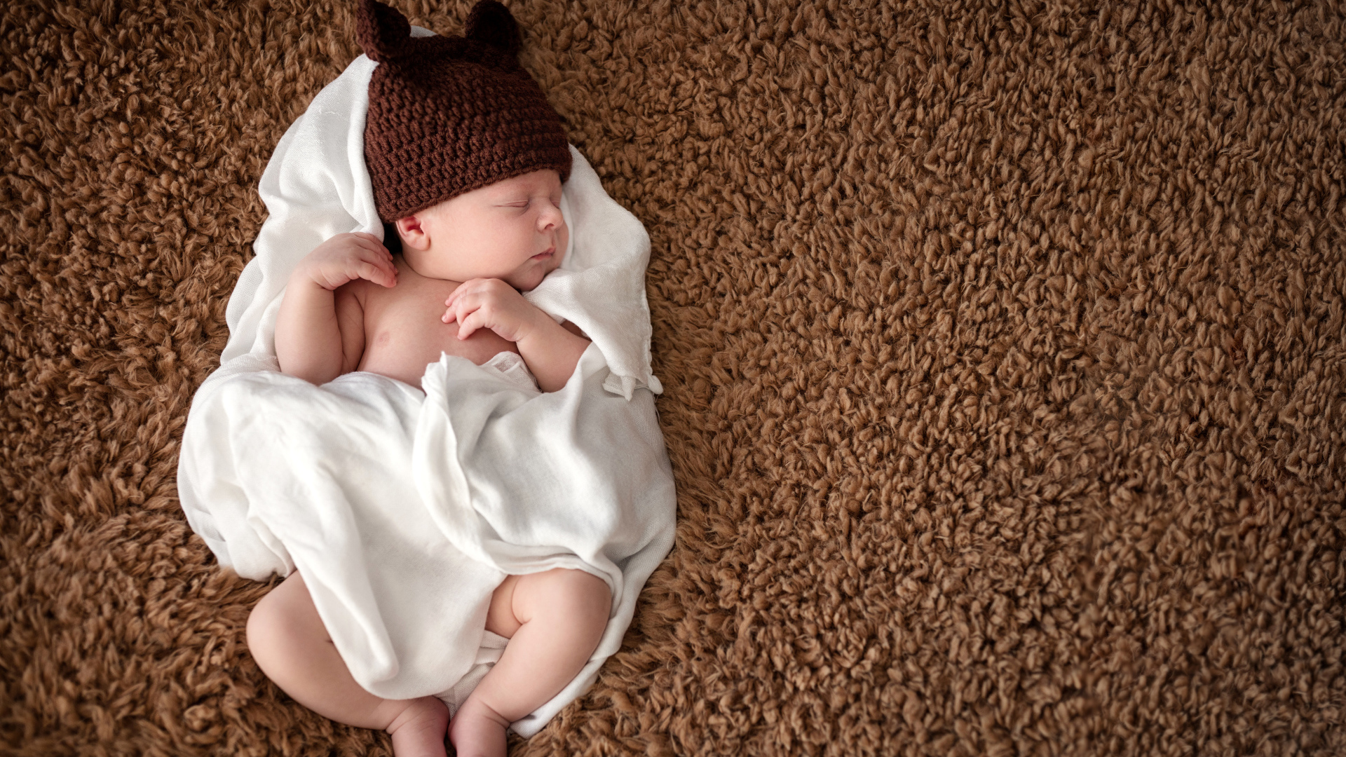 Младенец в коричневой вязаной шапке в белом покрывале 