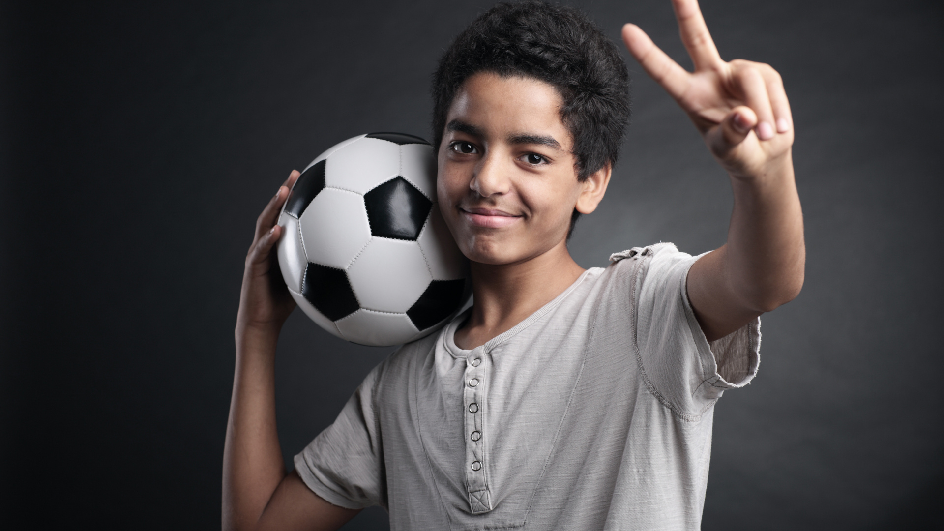 Мальчик с футбольным мячом на плече на сером фоне