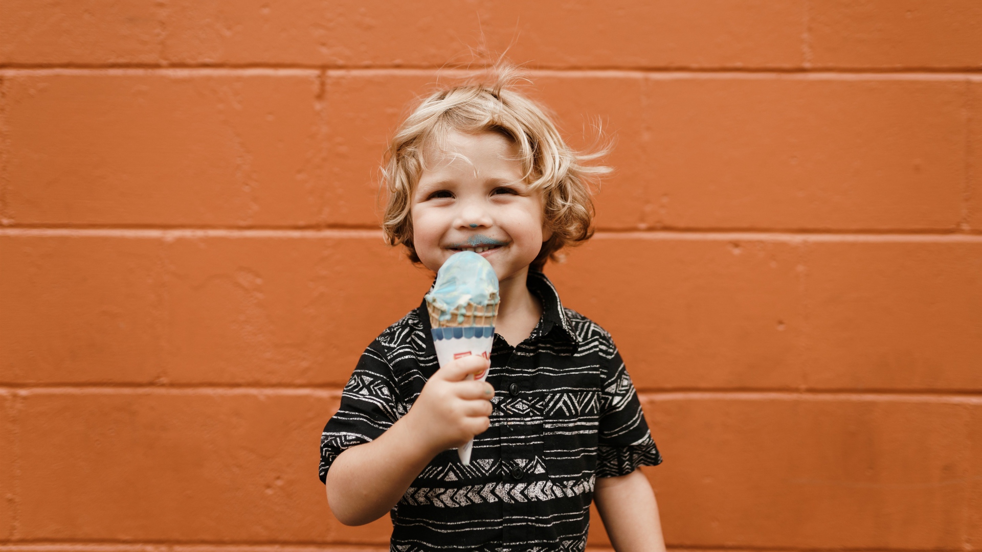Маленький мальчик с мороженым в руках у стены