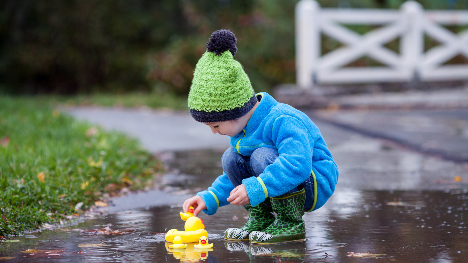 Маленький мальчик с резиновыми уточками в луже осенью
