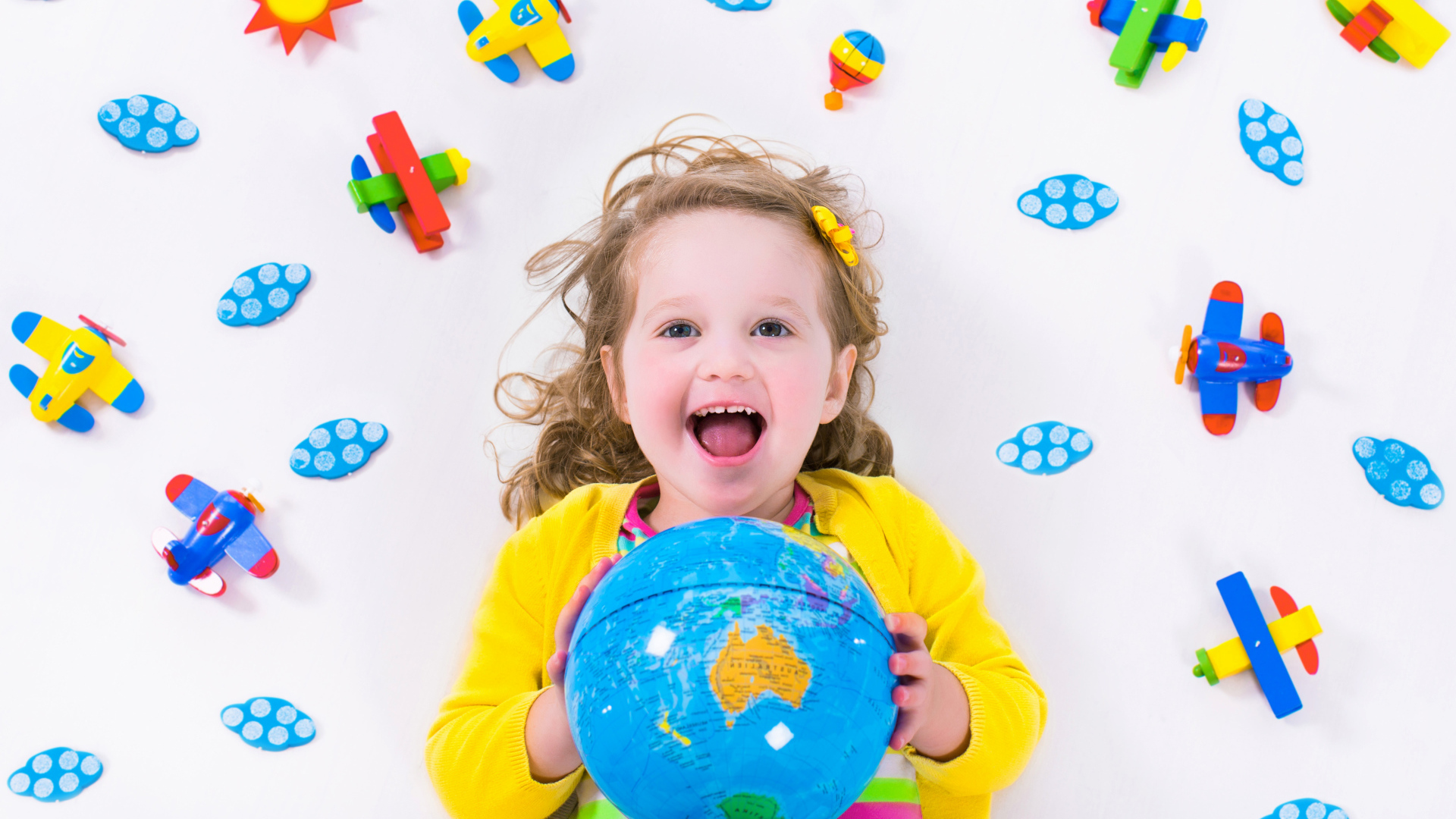 Маленькая веселая девочка с глобусом в руках 