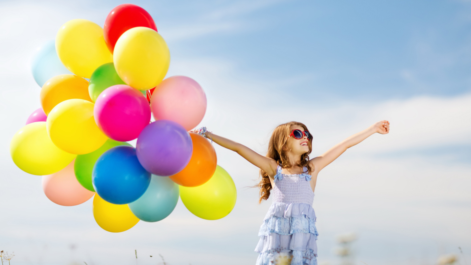 Маленькая девочка держит в руке много воздушных шаров