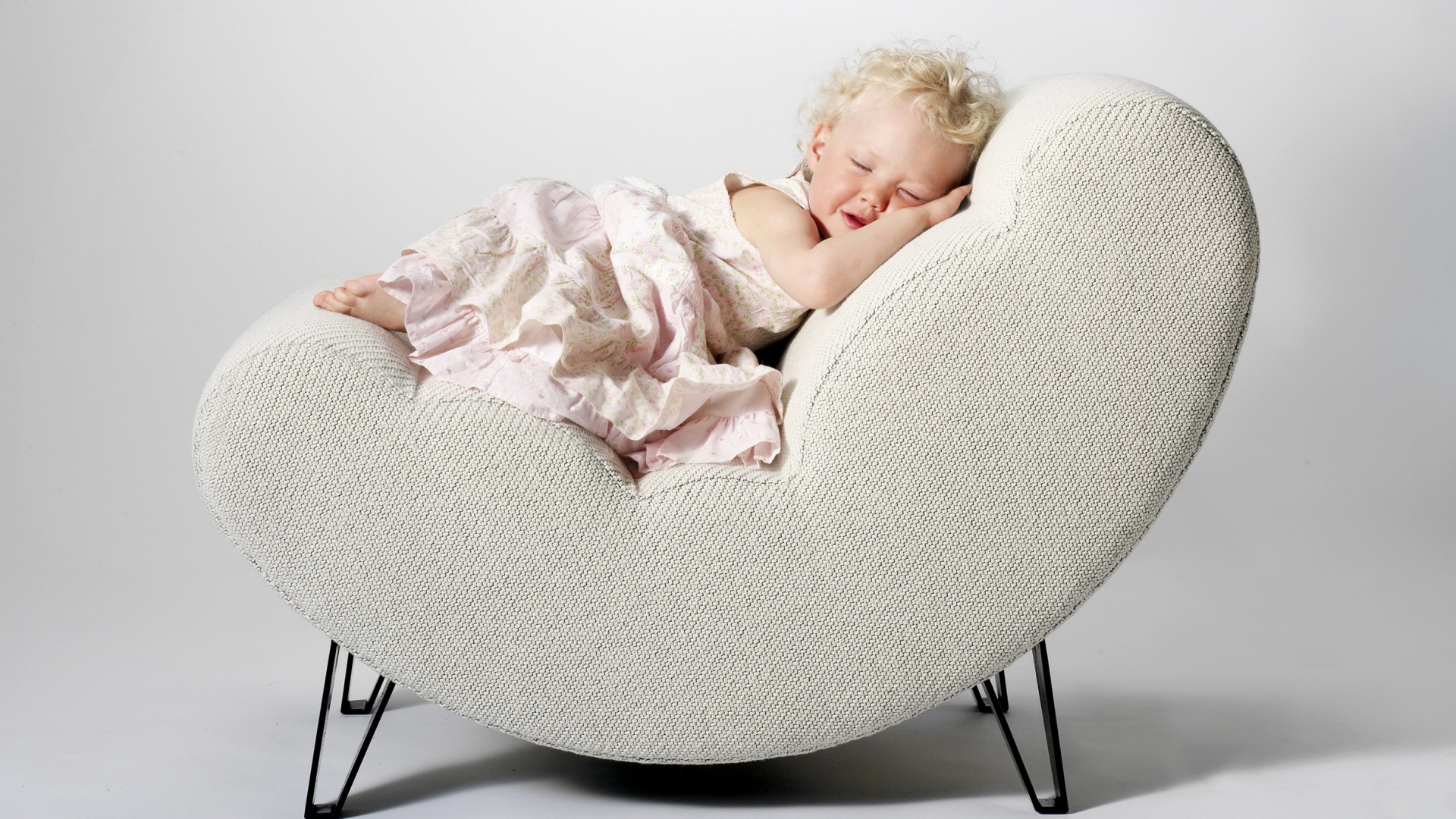 Маленькая девочка в розовом платье спит в кресле