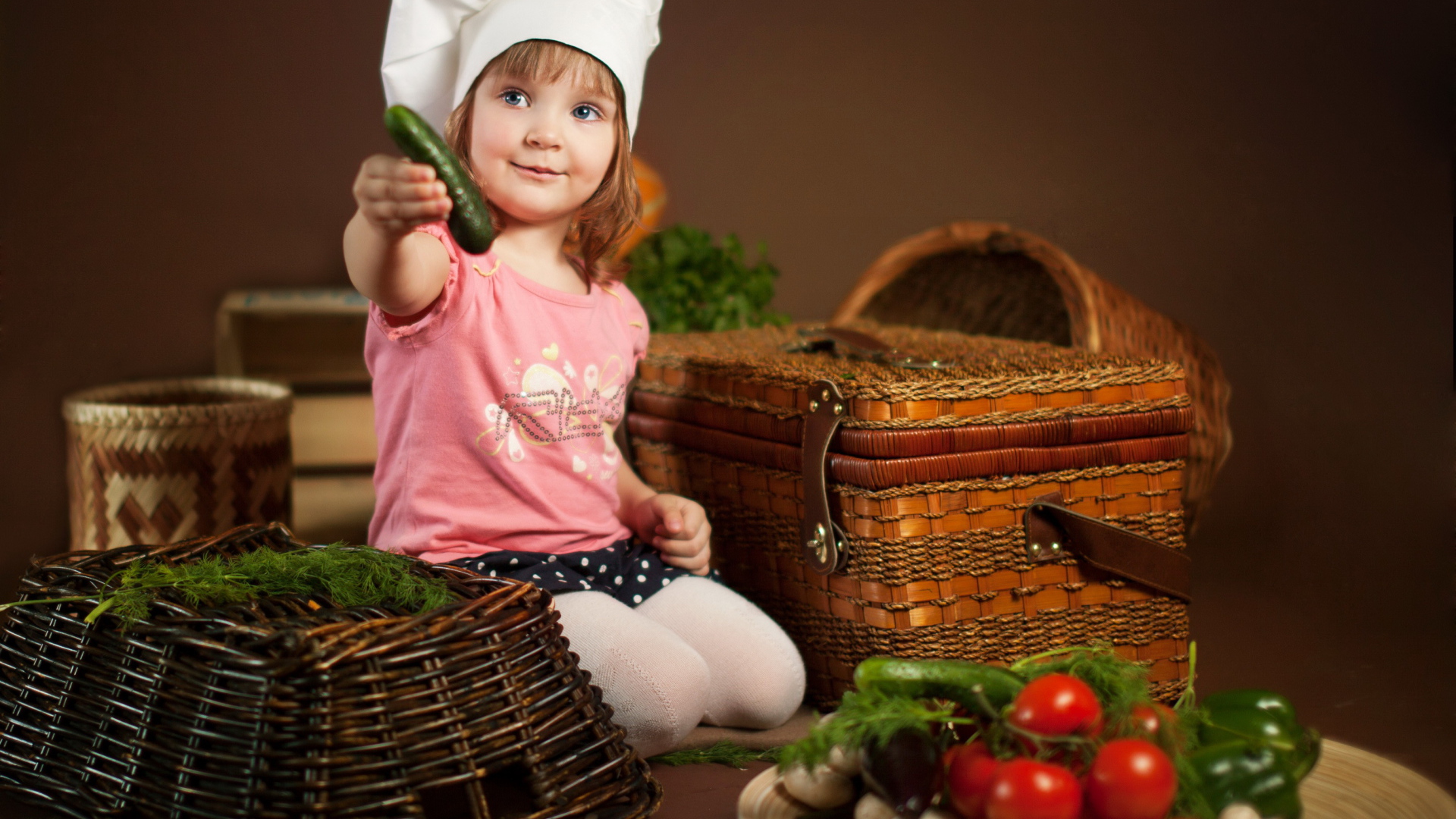 Маленькая девочка сидит на столе с корзинами и овощами