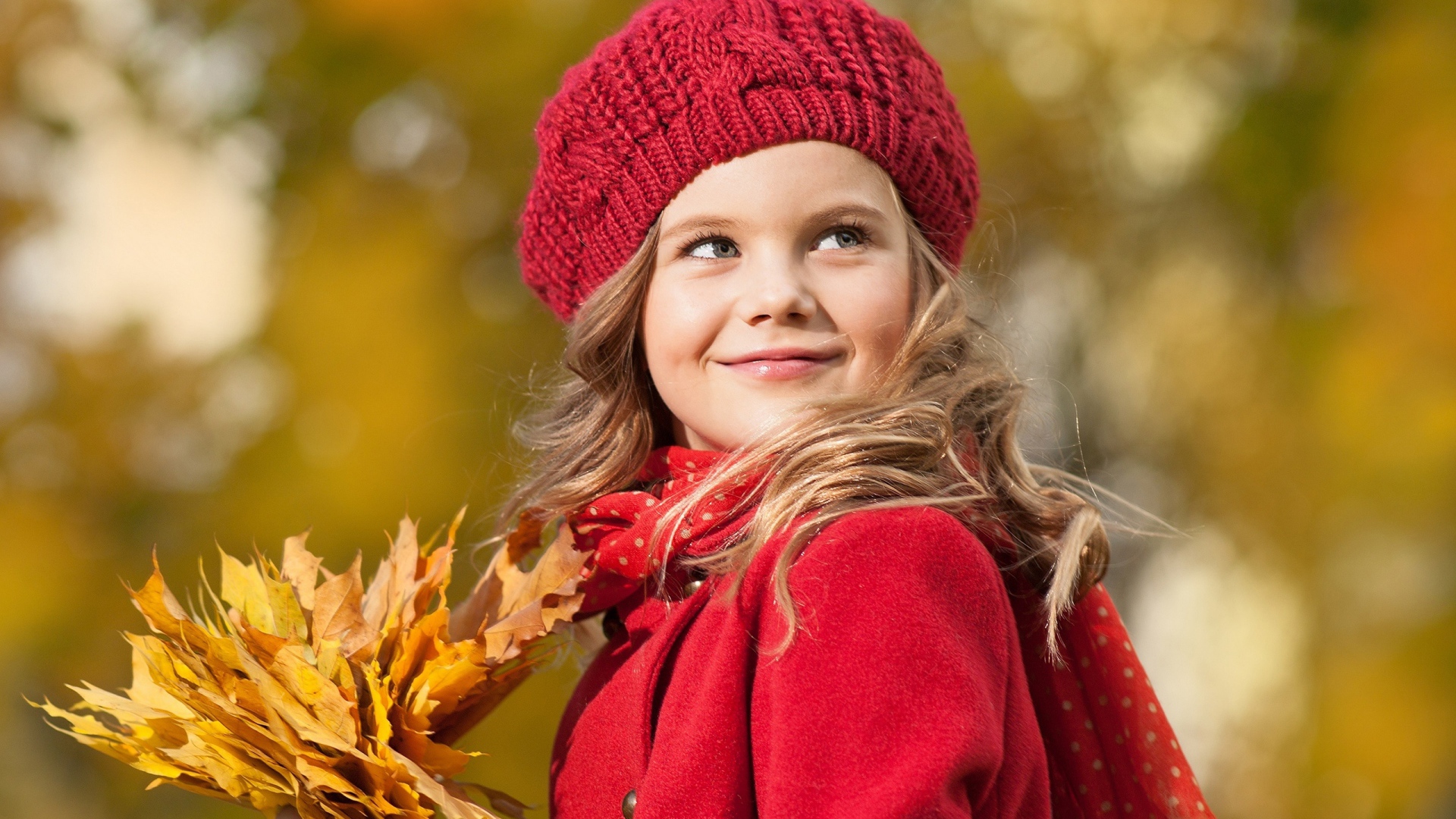 Маленькая девочка с желтыми листьями в руке осенью