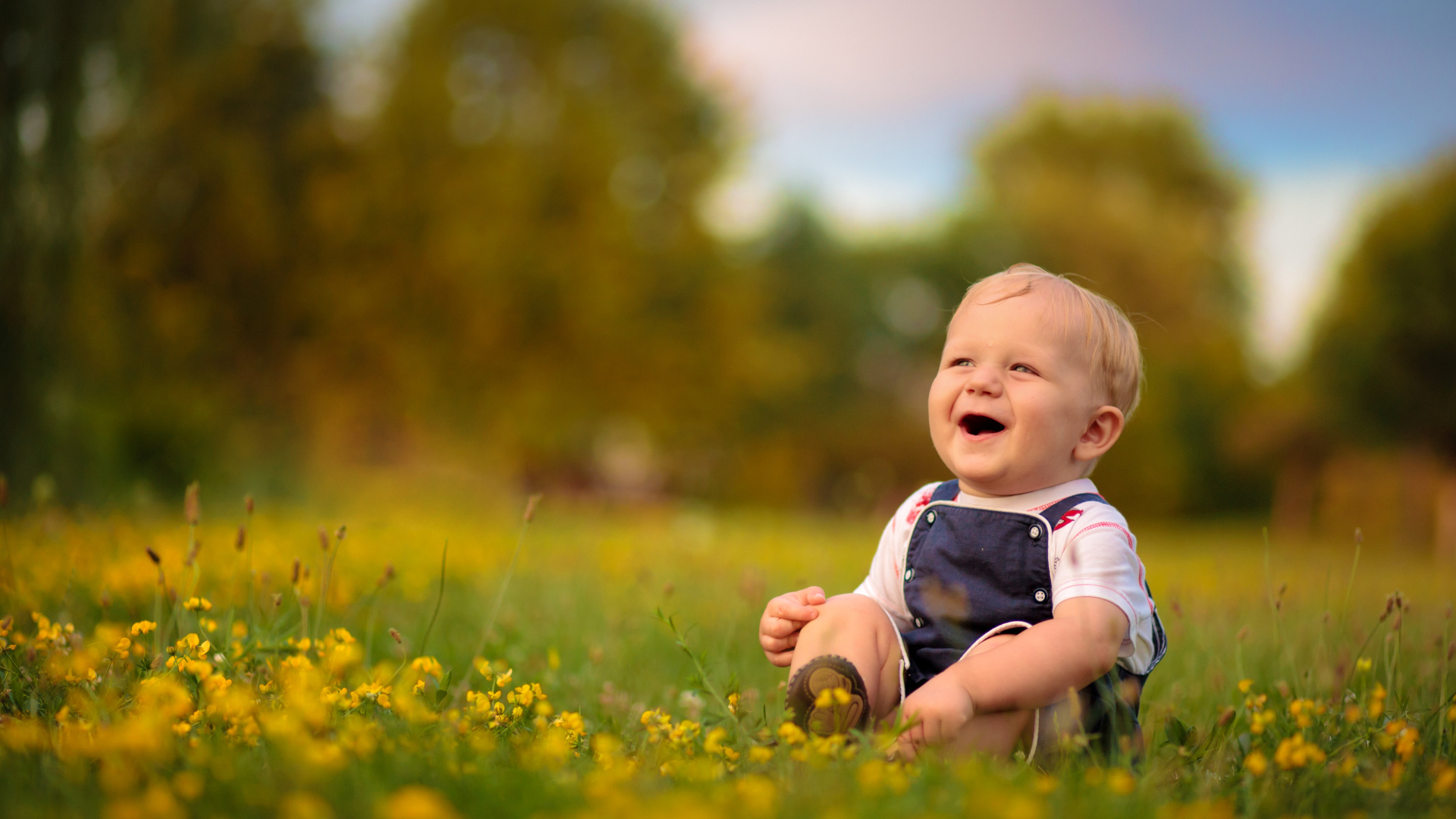 Маленький смеющийся мальчик сидит на траве с желтыми цветами