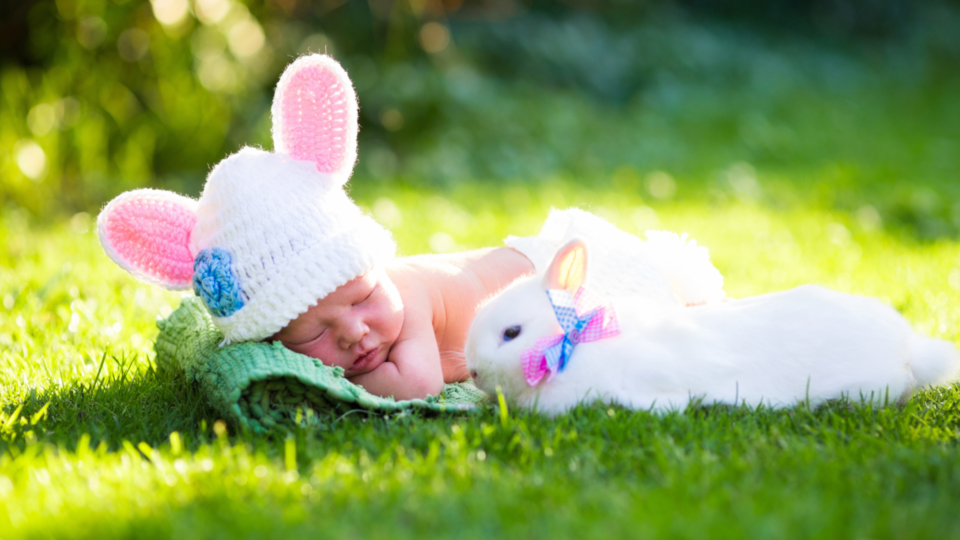 Маленький спящий грудной ребенок на зеленой траве с белым кроликом