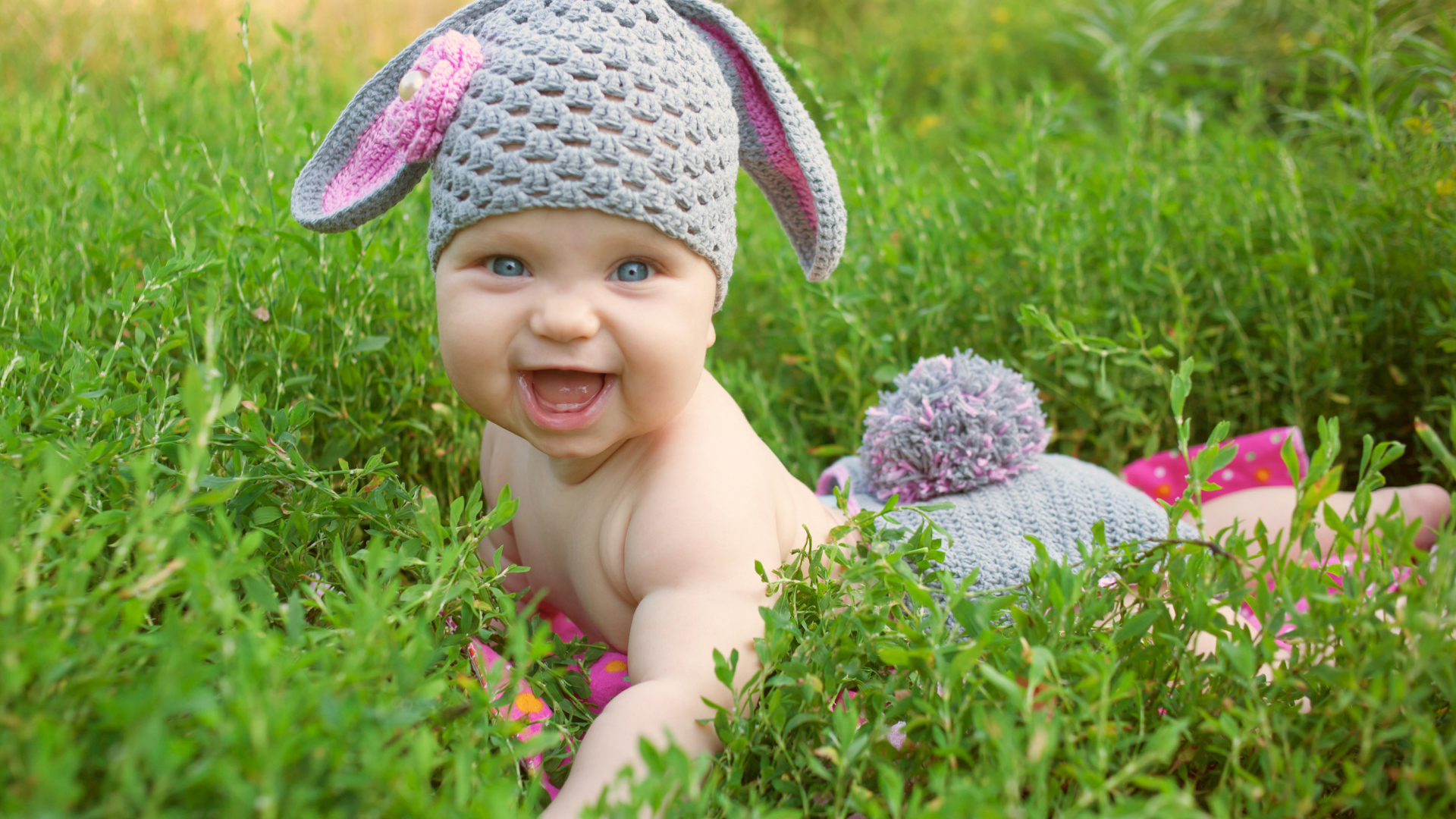 Маленький улыбающийся ребенок в костюме зайчика лежит в зеленой траве